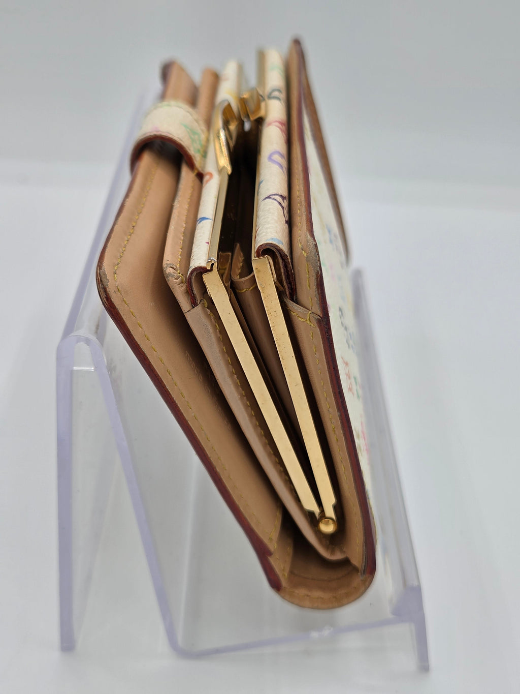 A brown leather wallet with gold-tone hardware and patterned paper inserts, displayed on a clear acrylic stand against a white background.
