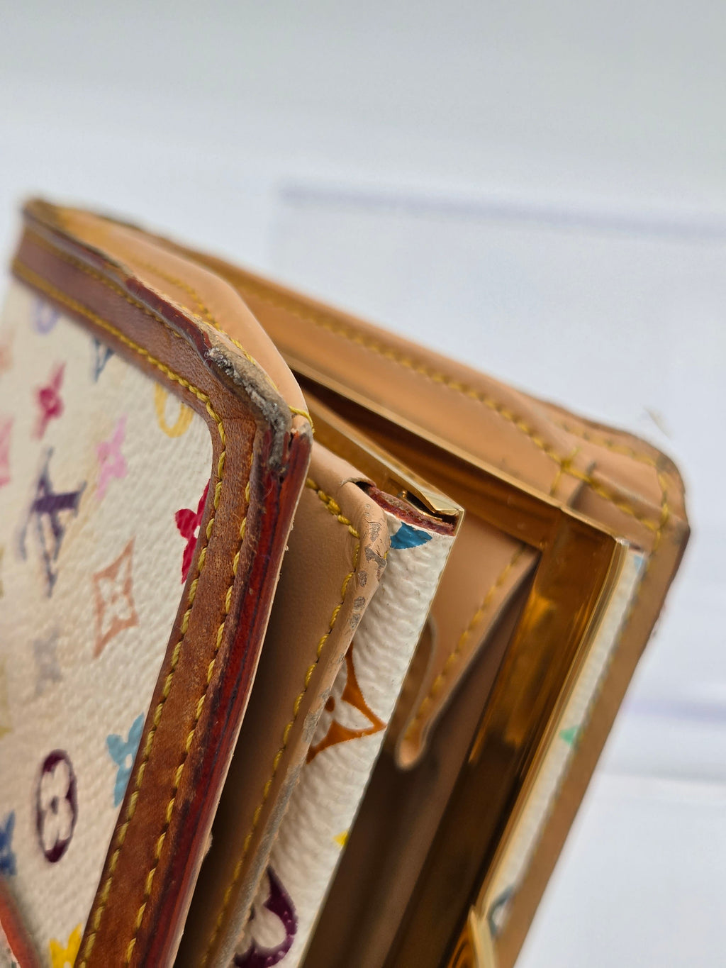 Close-up of a Louis Vuitton wallet in beige monogram canvas with brown leather trim and gold-tone metal card slots.