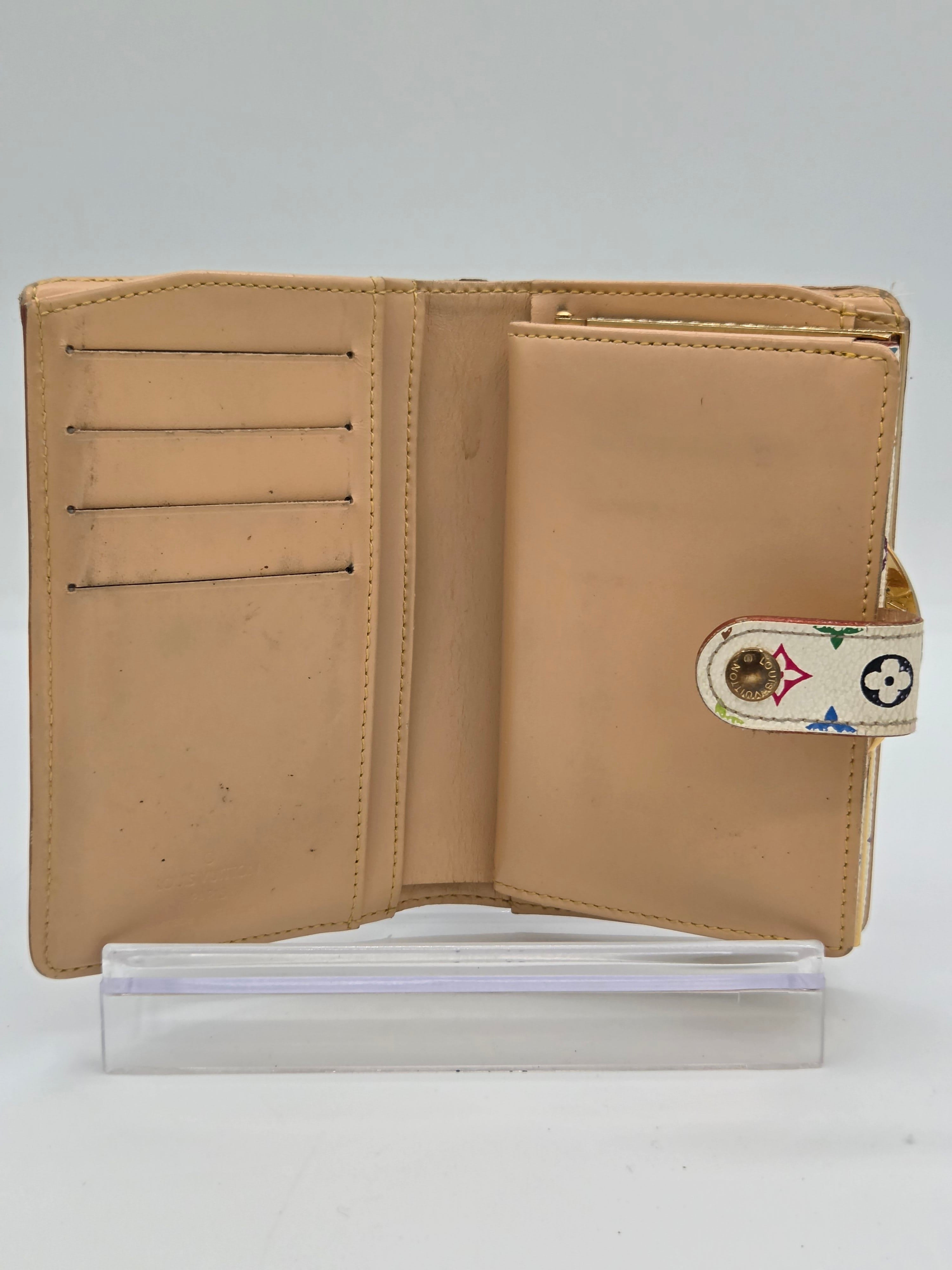 A beige leather wallet shown open, featuring multiple card slots, a top pocket, and a decorative strap closure with a small Louis Vuitton monogram motif. A clear plastic sleeve is positioned to the right of the wallet against a plain white background.