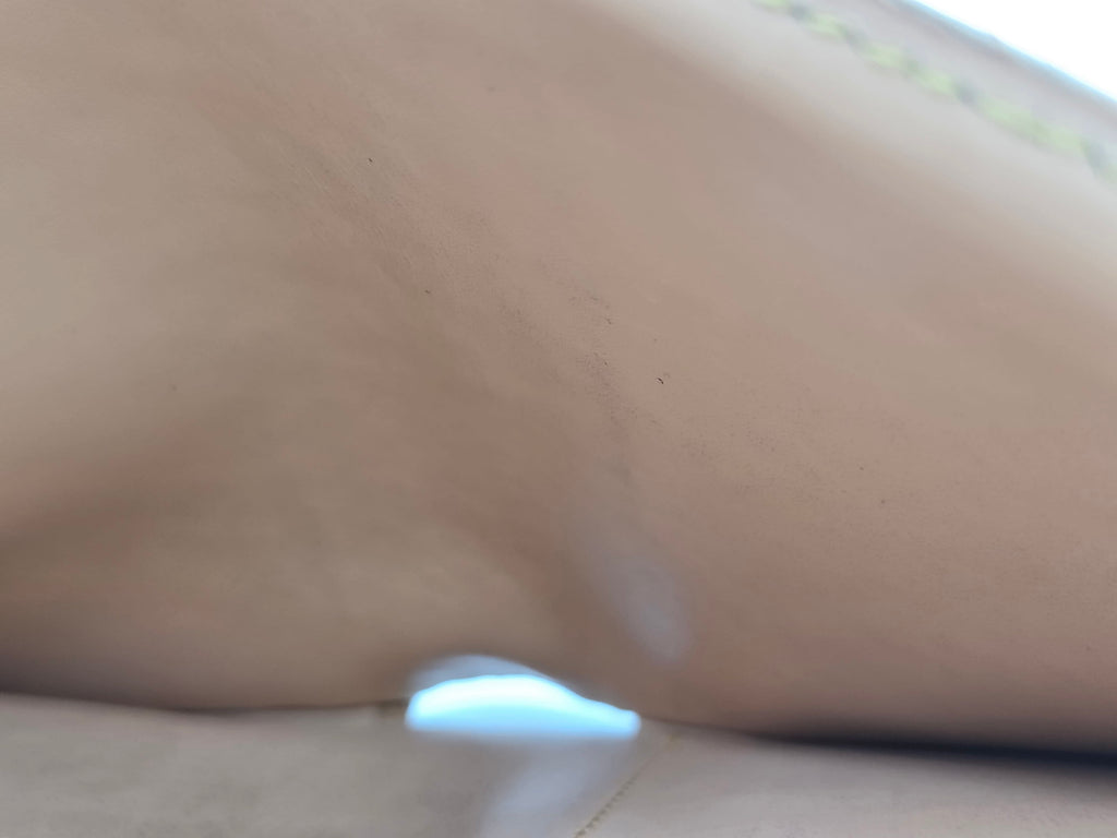 Close-up of a beige leather or faux-leather surface with a small light blue reflective highlight near the top center.