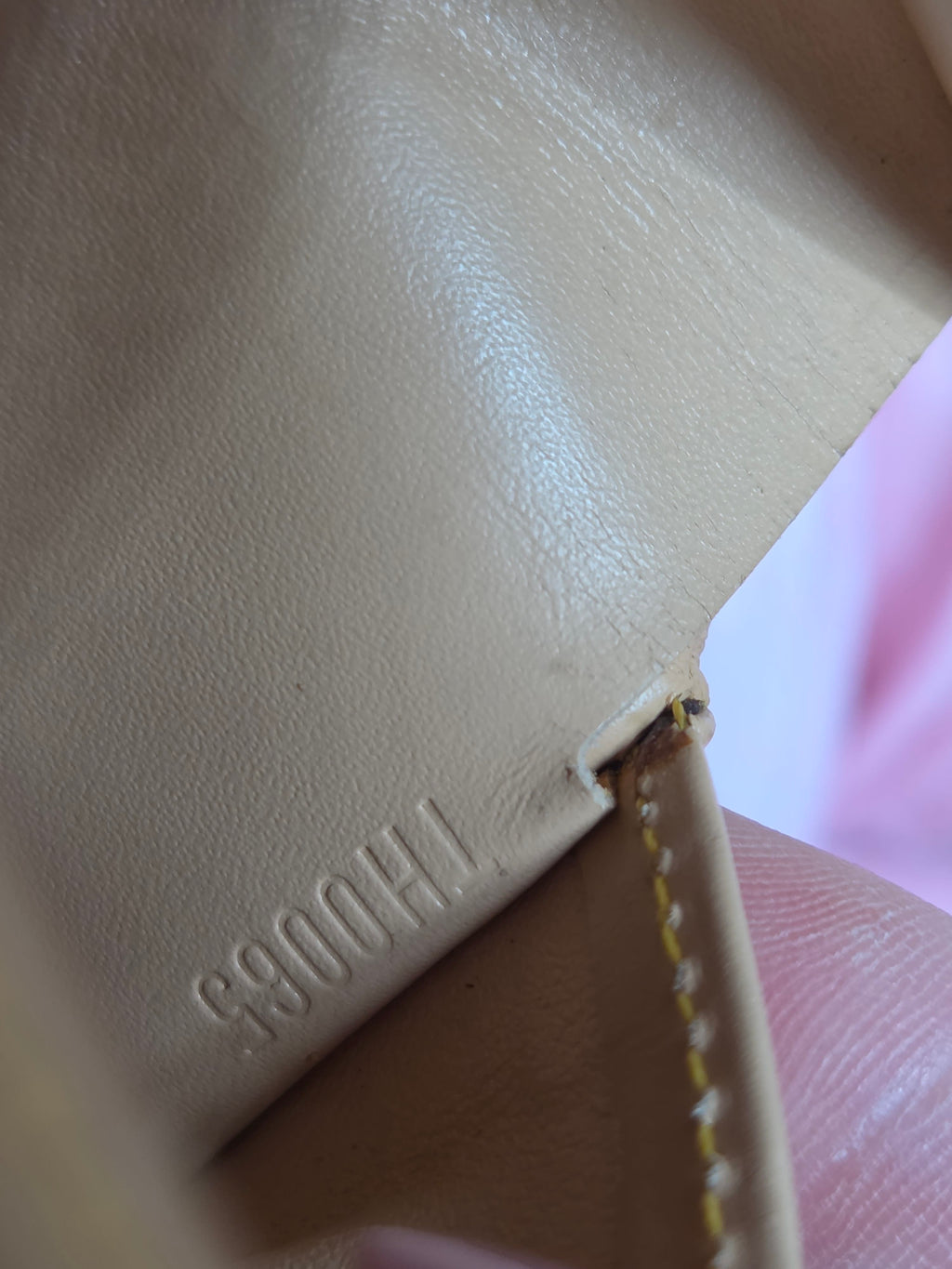 Close-up of a light beige leather item showing embossed stamped characters 'F390041' on the interior corner, a stitched edge, and a small pink fabric area in the background.