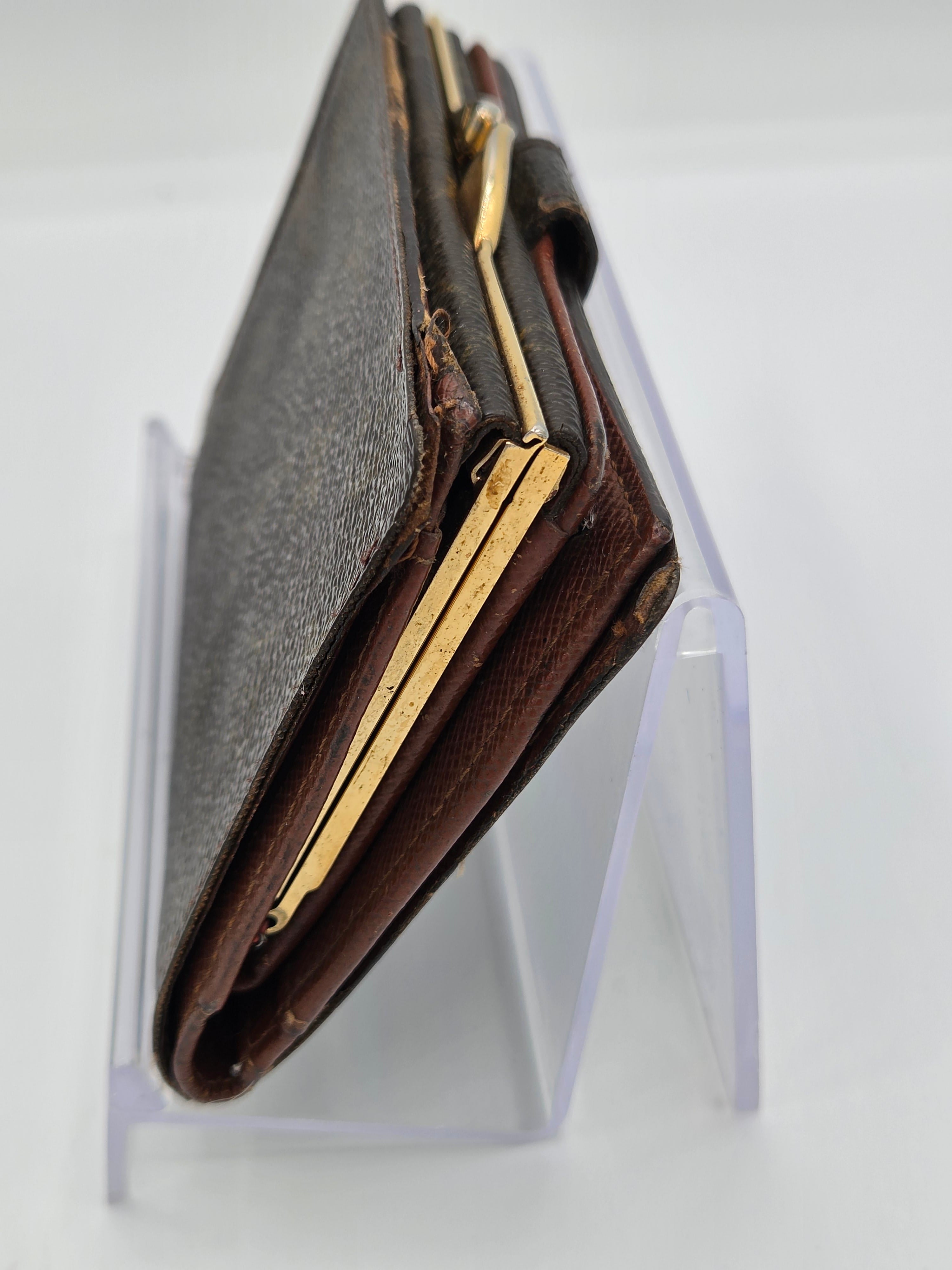 A vintage brown leather wallet with gold-tone metal trim, displayed on a clear acrylic stand against a white background.