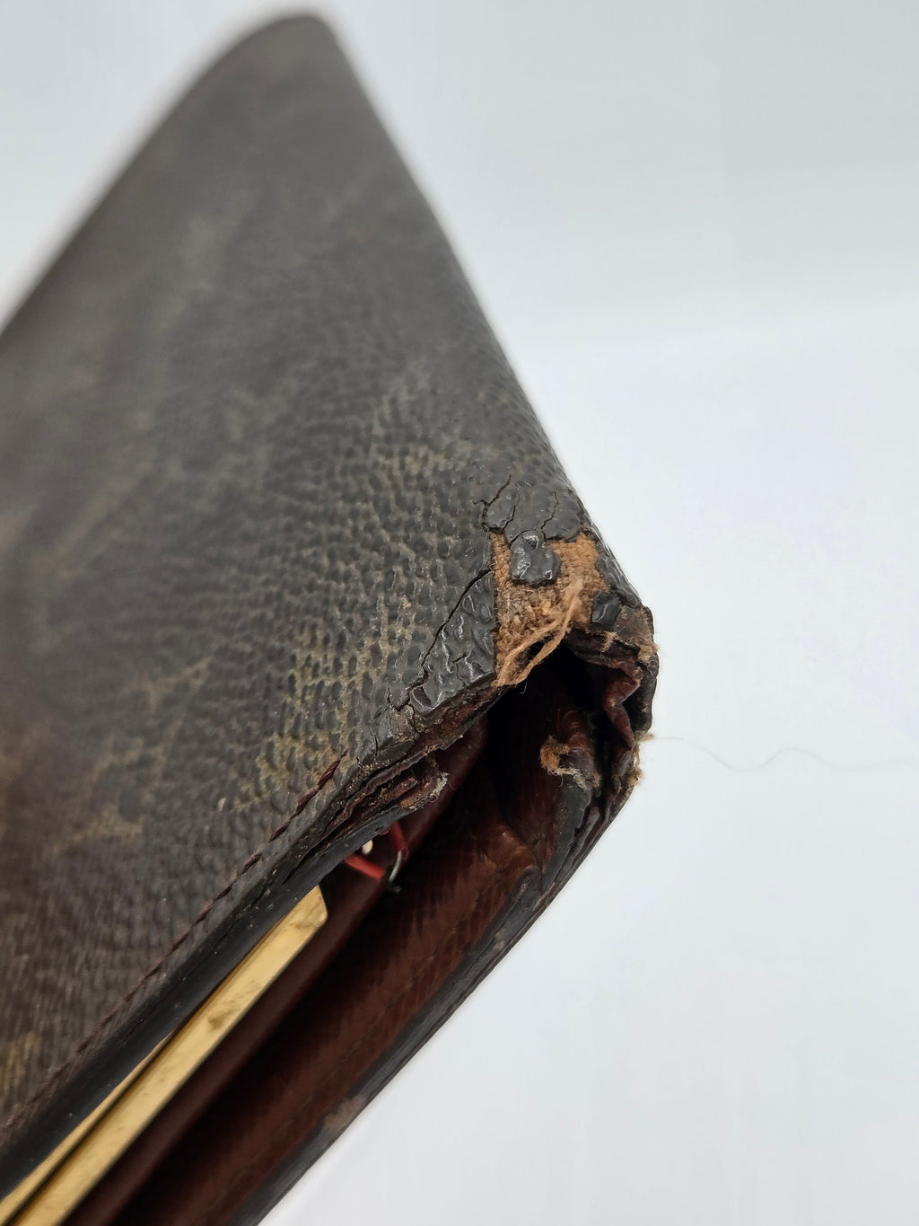 A close-up of a heavily worn brown leather wallet corner with severe tearing, frayed edges, and exposed interior layers on a plain white background.