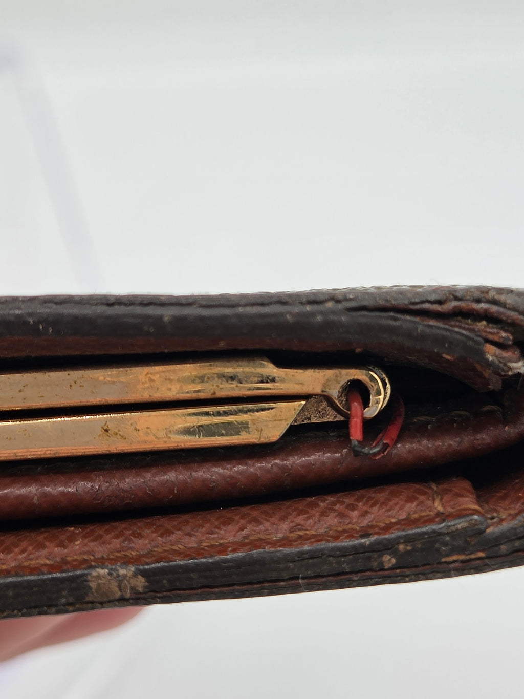 Close-up of a dark brown leather wallet or document holder with a brass keyring and a small red loop detail, set against a plain white background.
