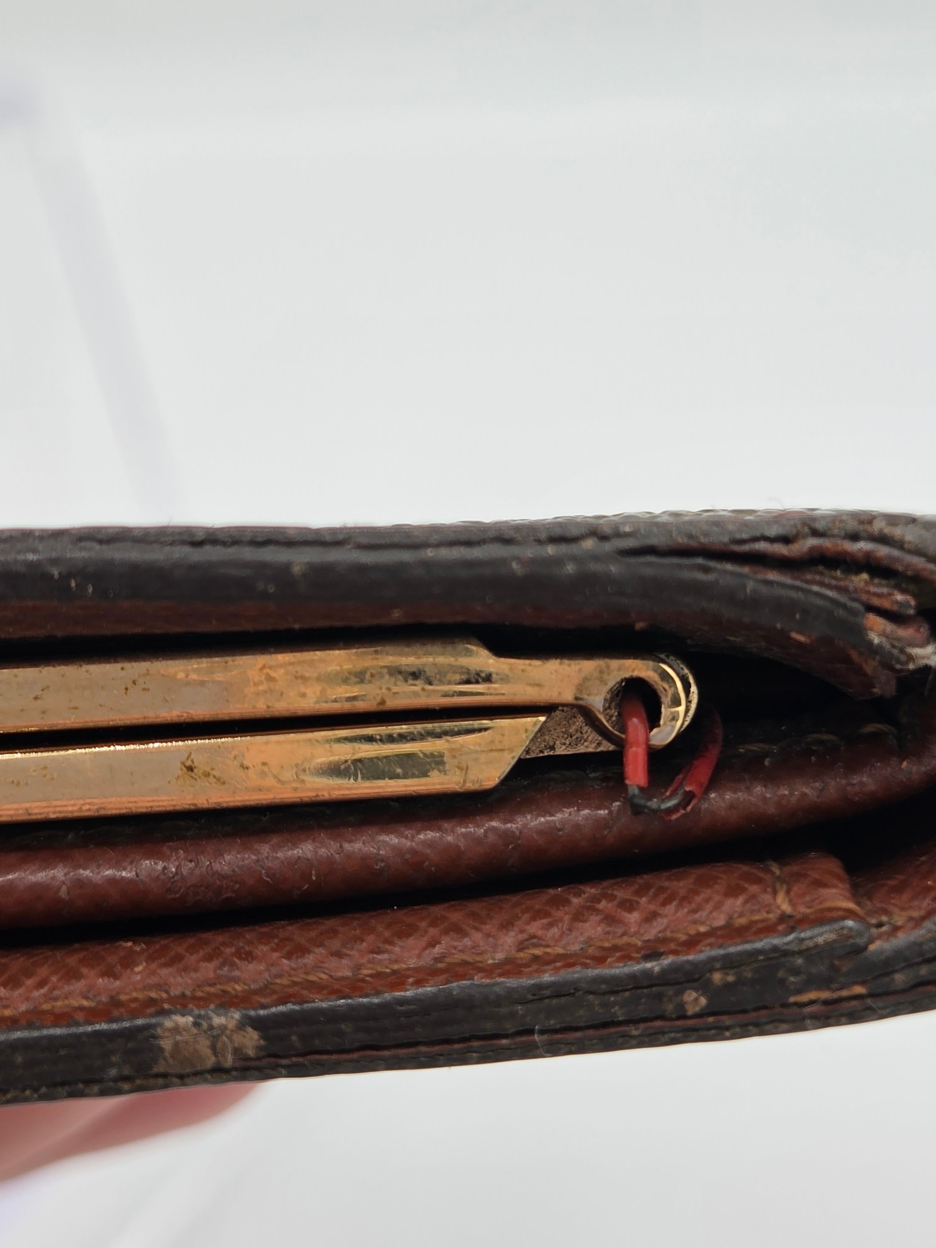 Close-up of a dark brown leather wallet or document holder with a brass keyring and a small red loop detail, set against a plain white background.