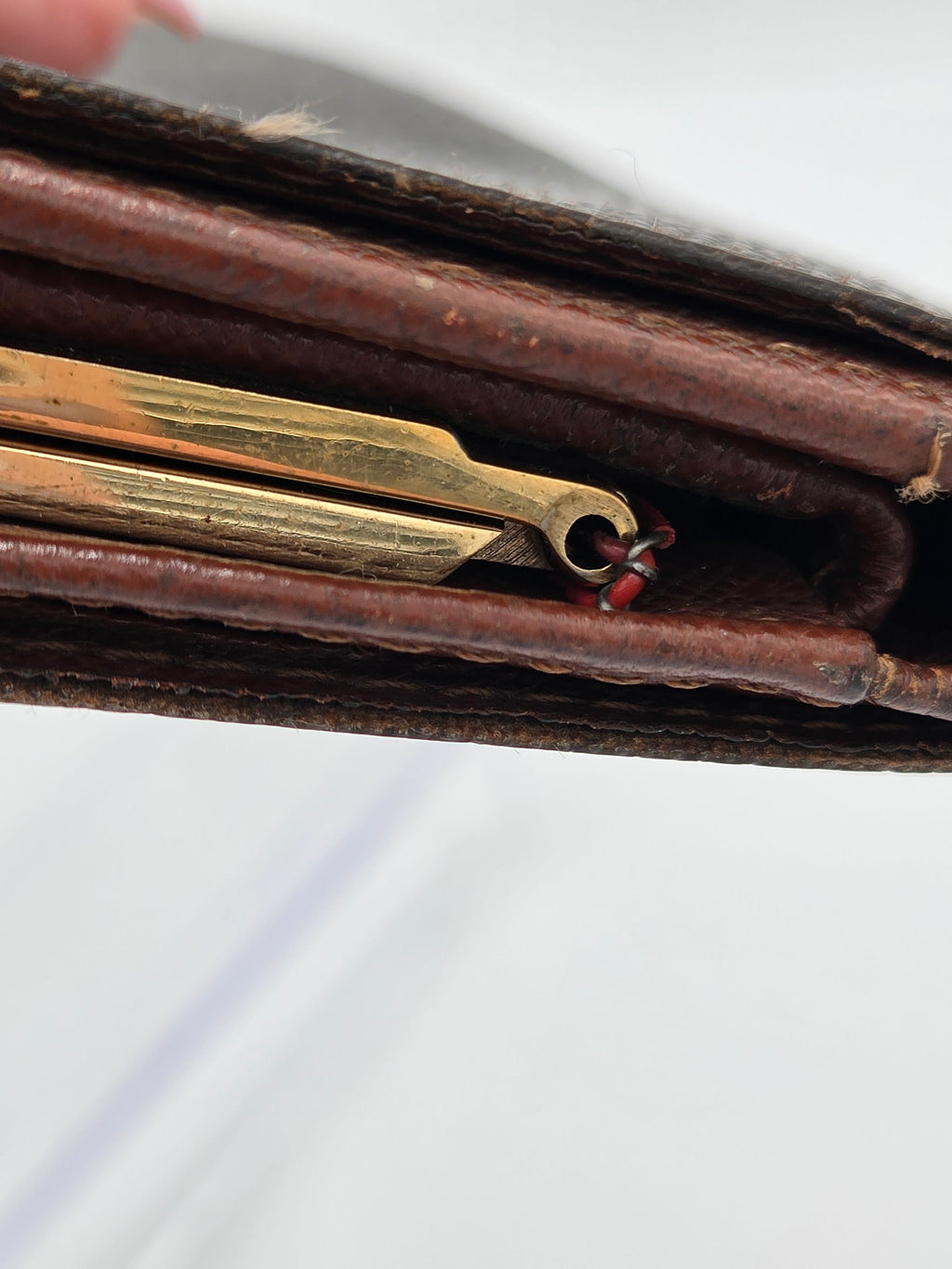 Close-up of a vintage brown leather case or wallet showing a brass-colored metal tool or charm hanging from the zipper area, with a white background.