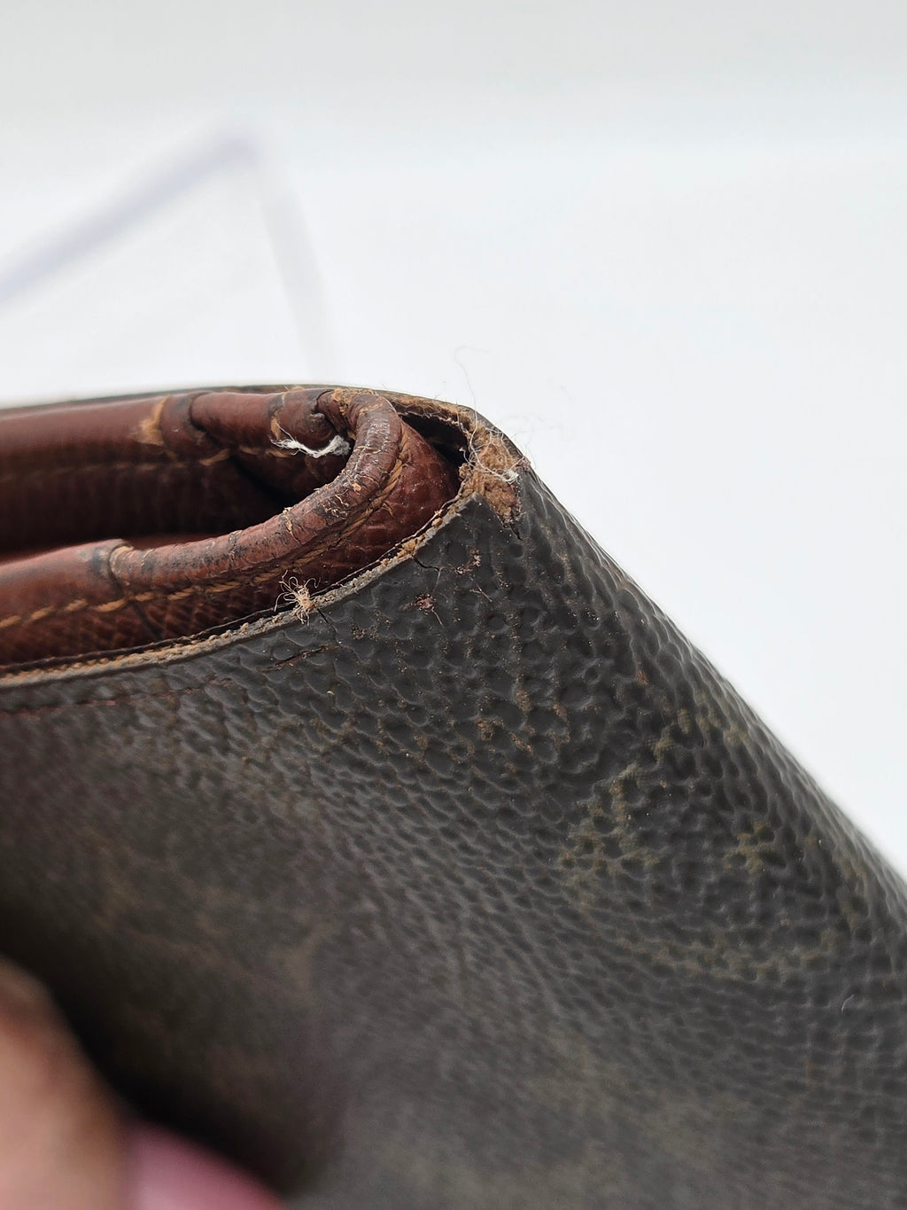 A close-up of a dark brown textured leather wallet corner showing significant wear, scuffing, and frayed edges.