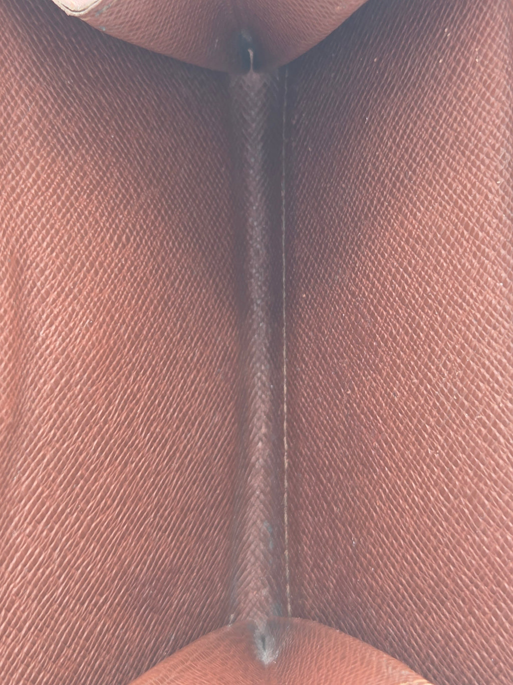 Close-up of a brown textured fabric or leather material with a stitched horizontal seam running through the center.