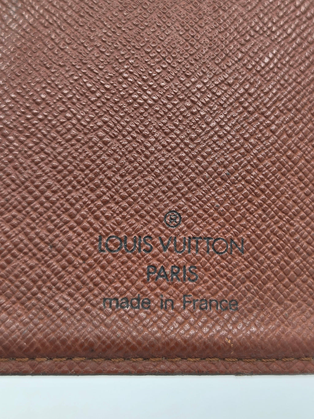 Close-up of a brown Louis Vuitton textured leather surface with embossed branding reading 'LOUIS VUITTON PARIS made in France'.