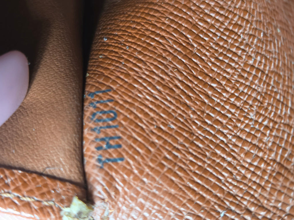 Close-up of a brown textured leather item showing a blue Louis Vuitton stamp and part of a finger holding it.