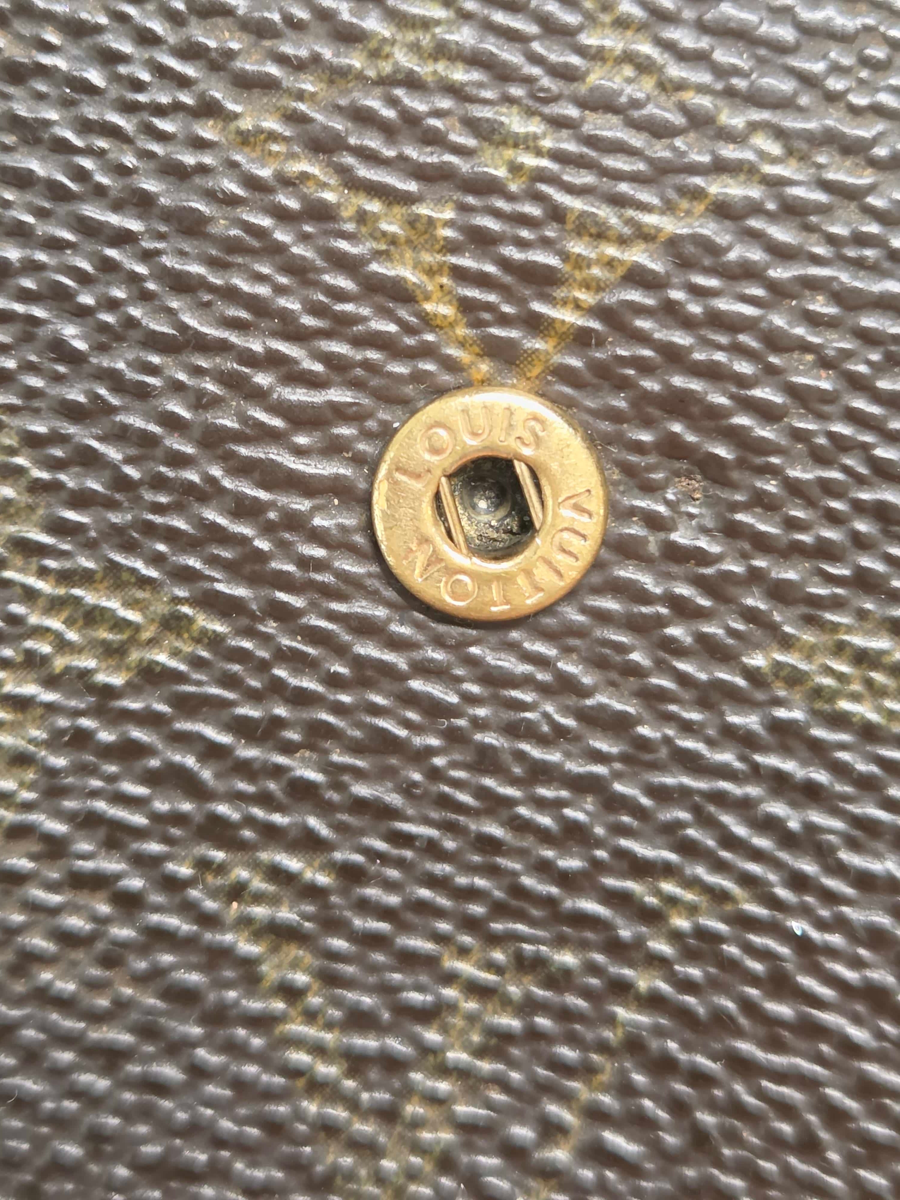 Close-up of a Louis Vuitton monogram canvas surface with a gold-tone metal snap button showing the brand name.