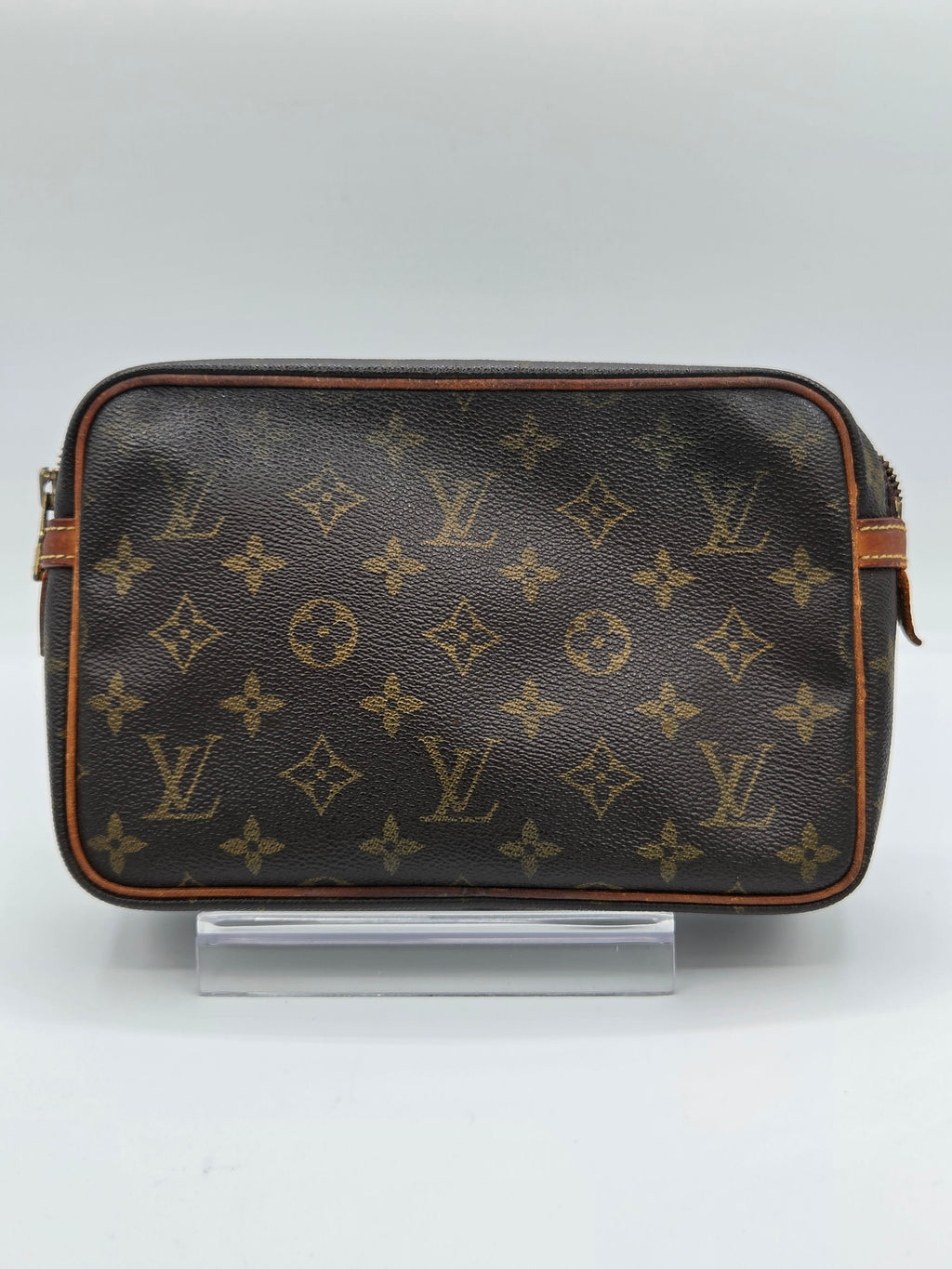 A Louis Vuitton monogram canvas toiletry bag in dark brown with tan leather trim, shown against a plain light gray background.