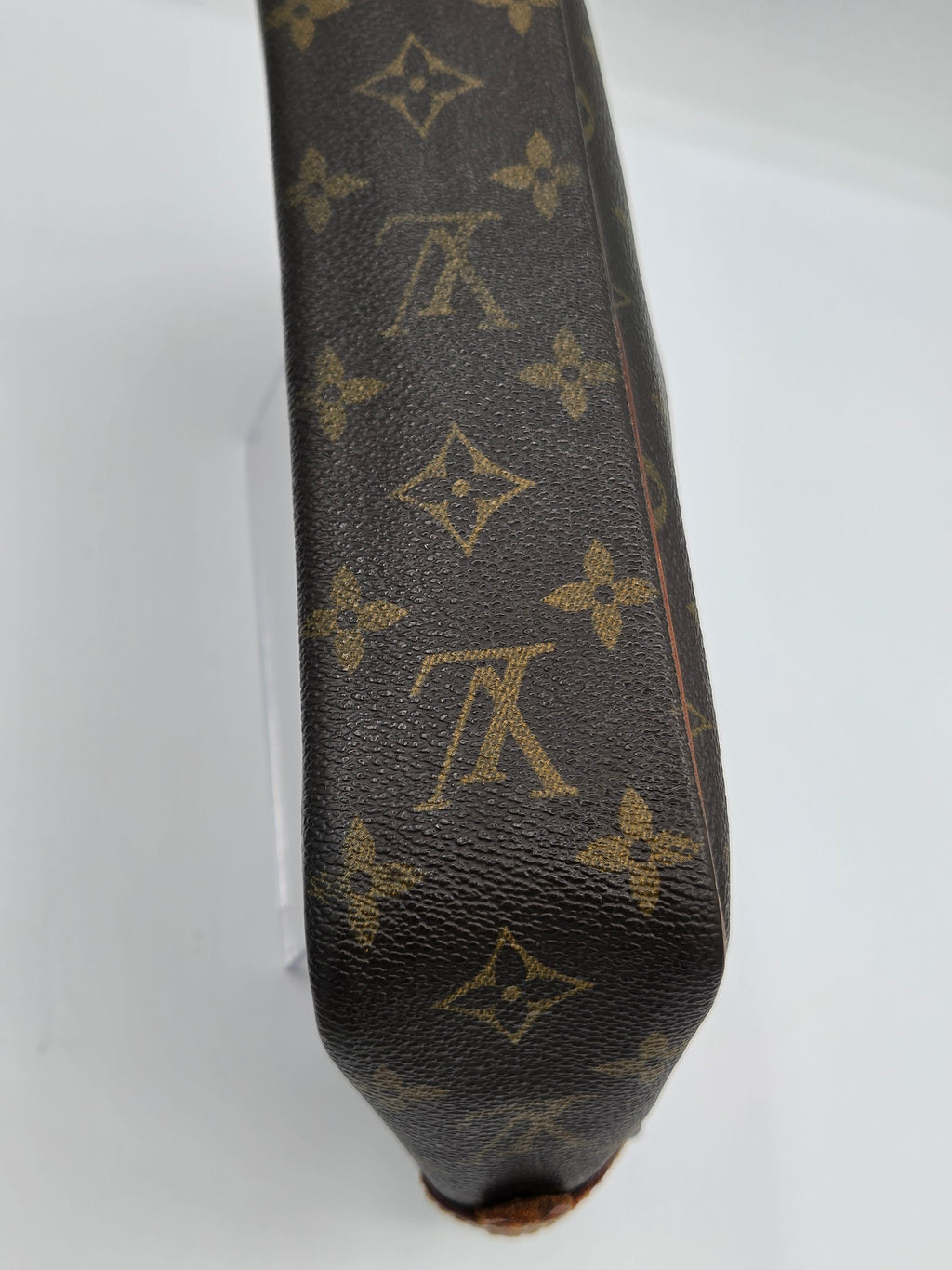 Close-up of a Louis Vuitton monogram canvas item, showing the classic dark brown background with tan LV logos and floral motifs.