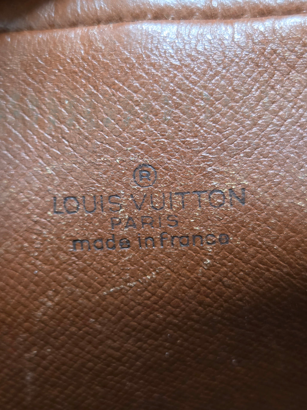 Close-up of a brown textured leather surface with embossed Louis Vuitton Paris made in France text.