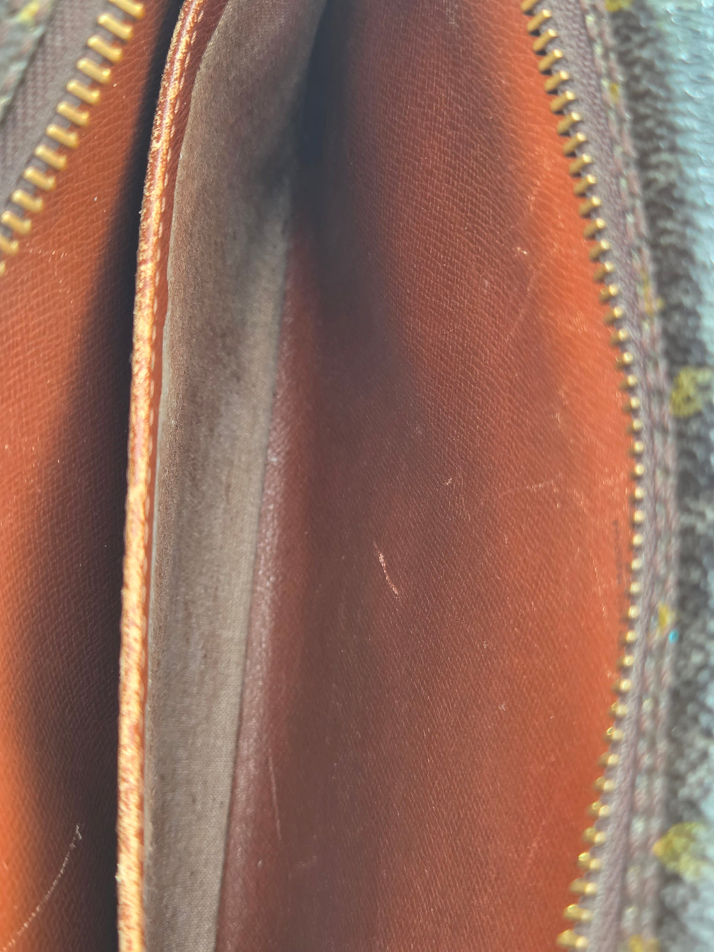 Close-up of the interior of a brown leather zippered pouch or wallet, showing the tan leather trim and gold-toned zipper teeth.