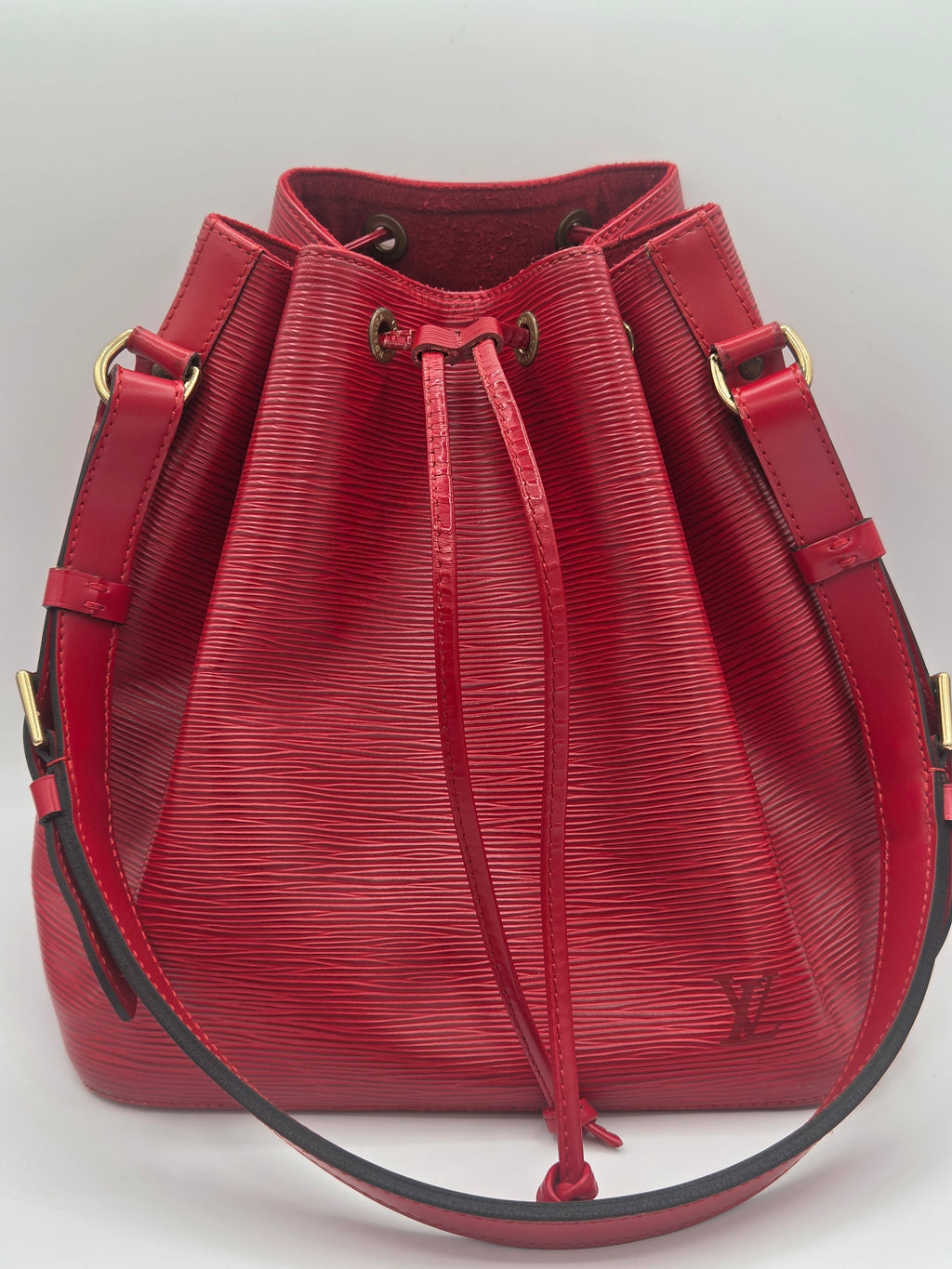 A red textured leather bucket bag with gold-tone hardware and a drawstring closure, shown from a top-down angle on a light background.