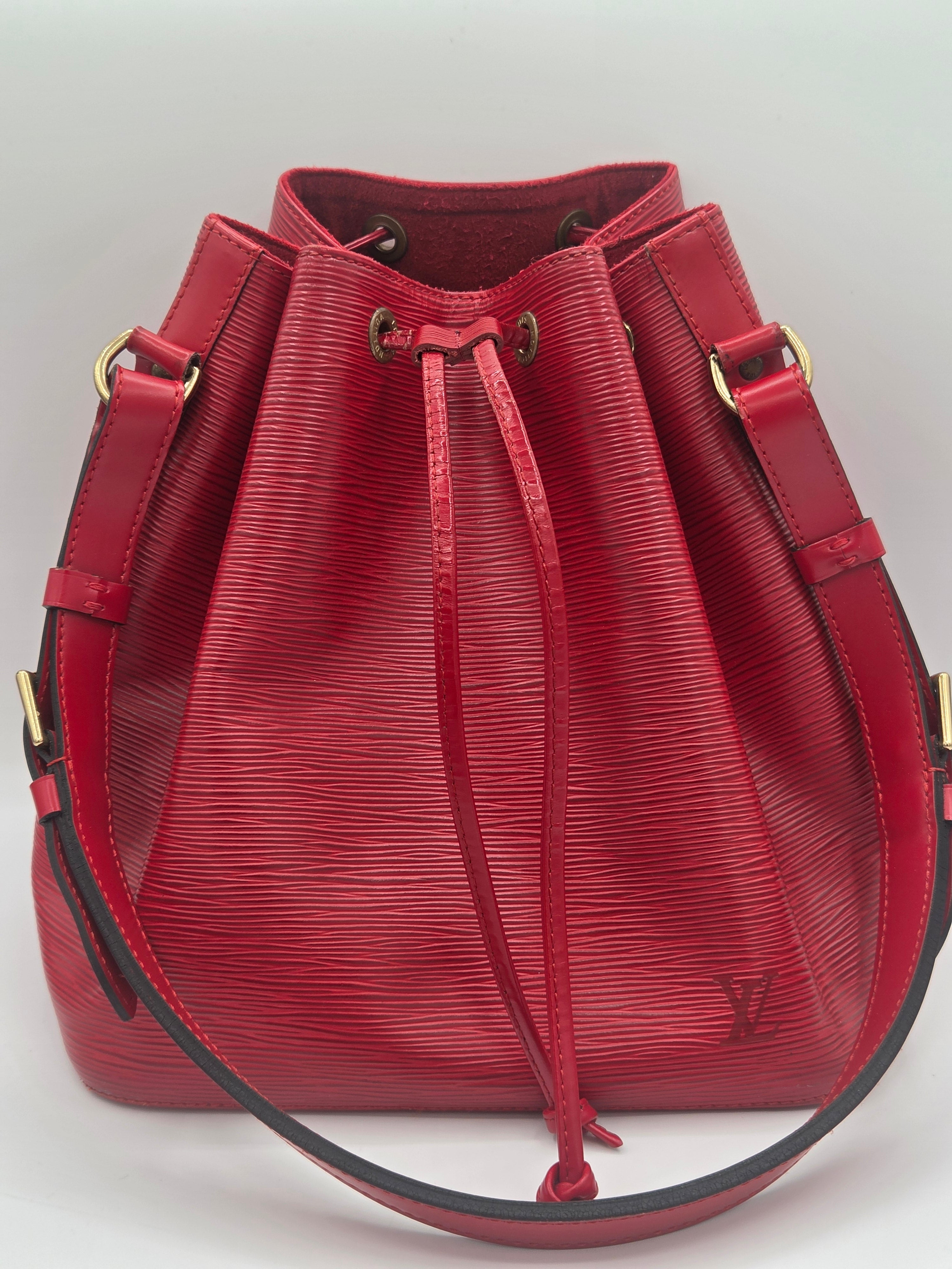 A red textured leather bucket bag with gold-tone hardware and a drawstring closure, shown from a top-down angle on a light background.