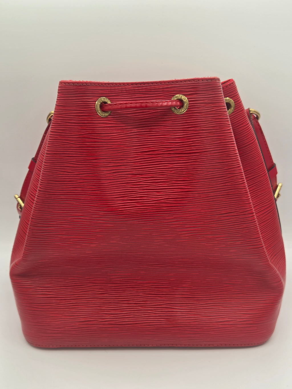 A red textured leather bucket bag with gold-tone hardware, shown from a top-down angle on a plain light background.