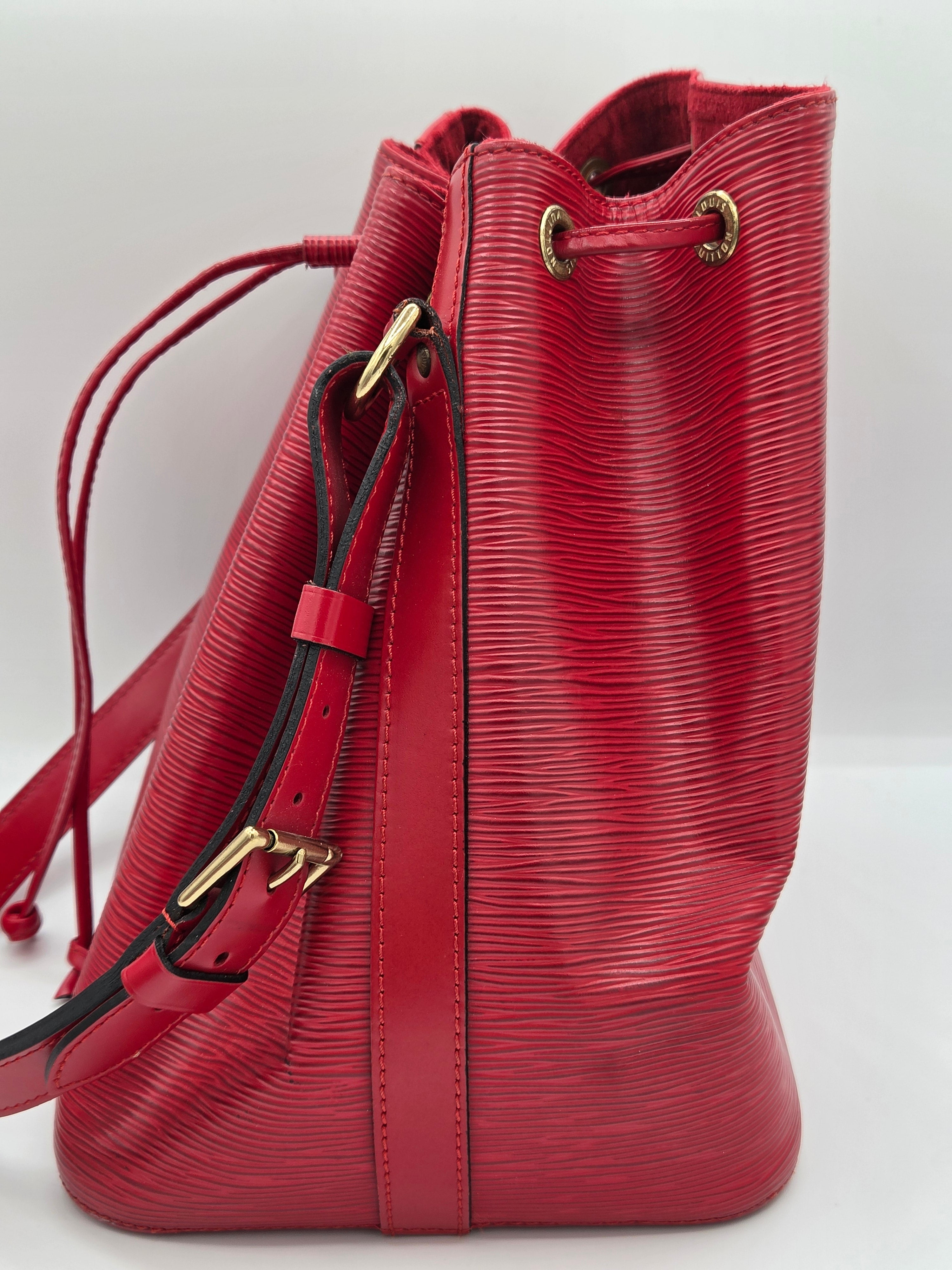 A red textured leather drawstring handbag with gold-tone hardware and a black-and-red strap detail, shown against a plain light background.