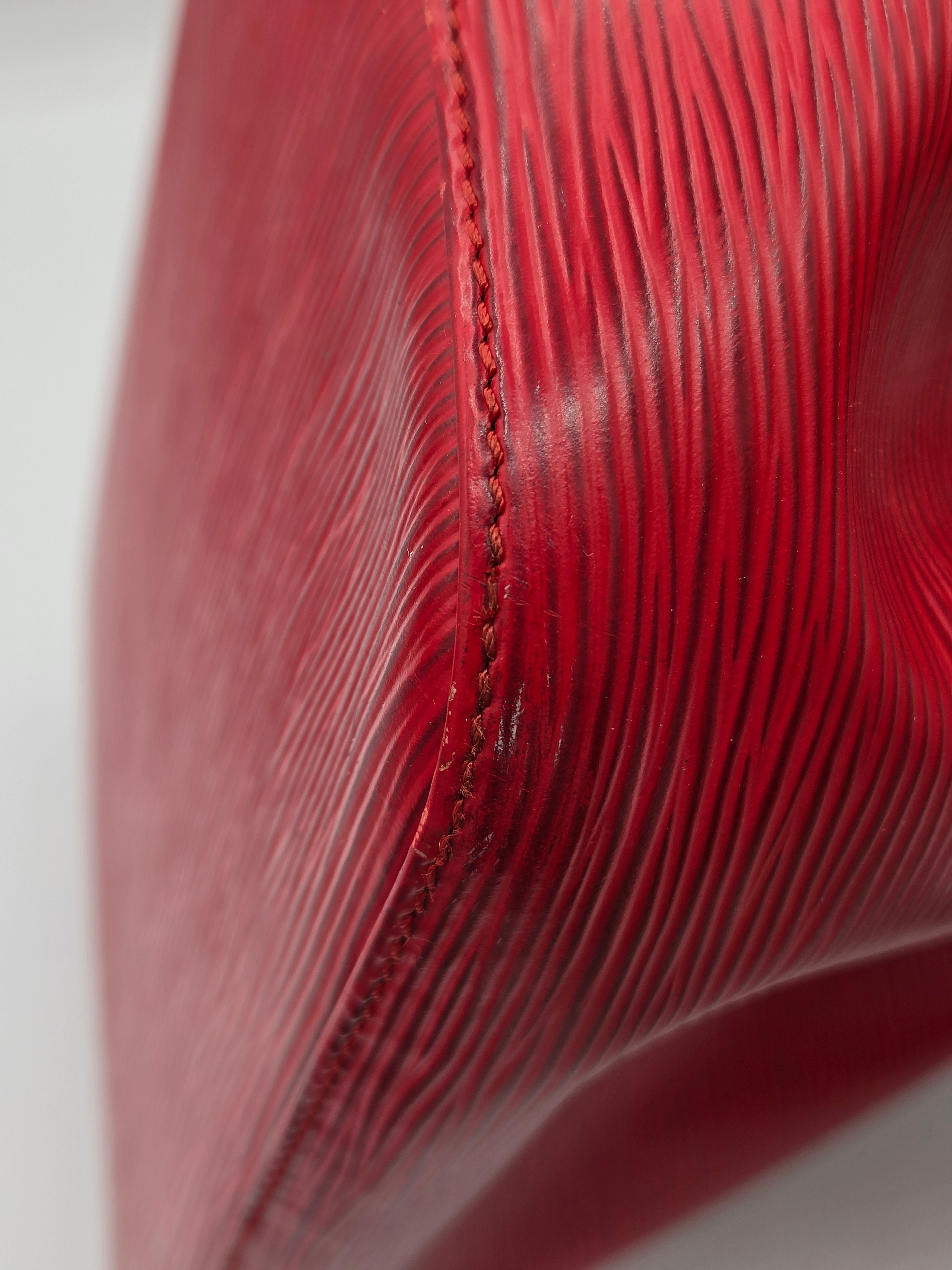 Close-up of a textured red leather product, showing fine grain and a stitched seam against a light gray background.