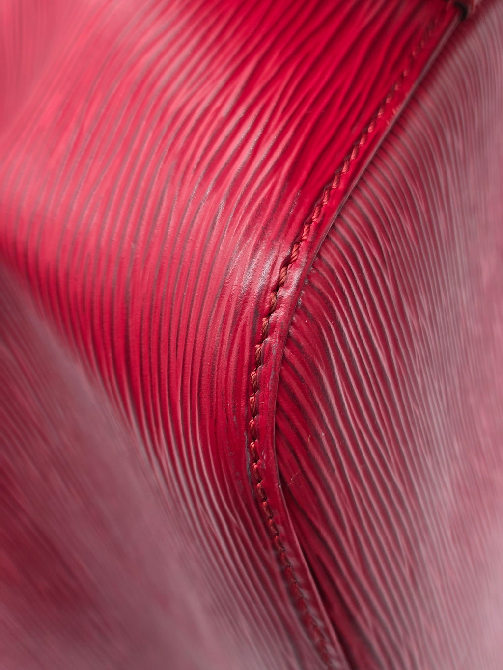 Close-up of a textured red leather surface with fine horizontal grain and a stitched seam.