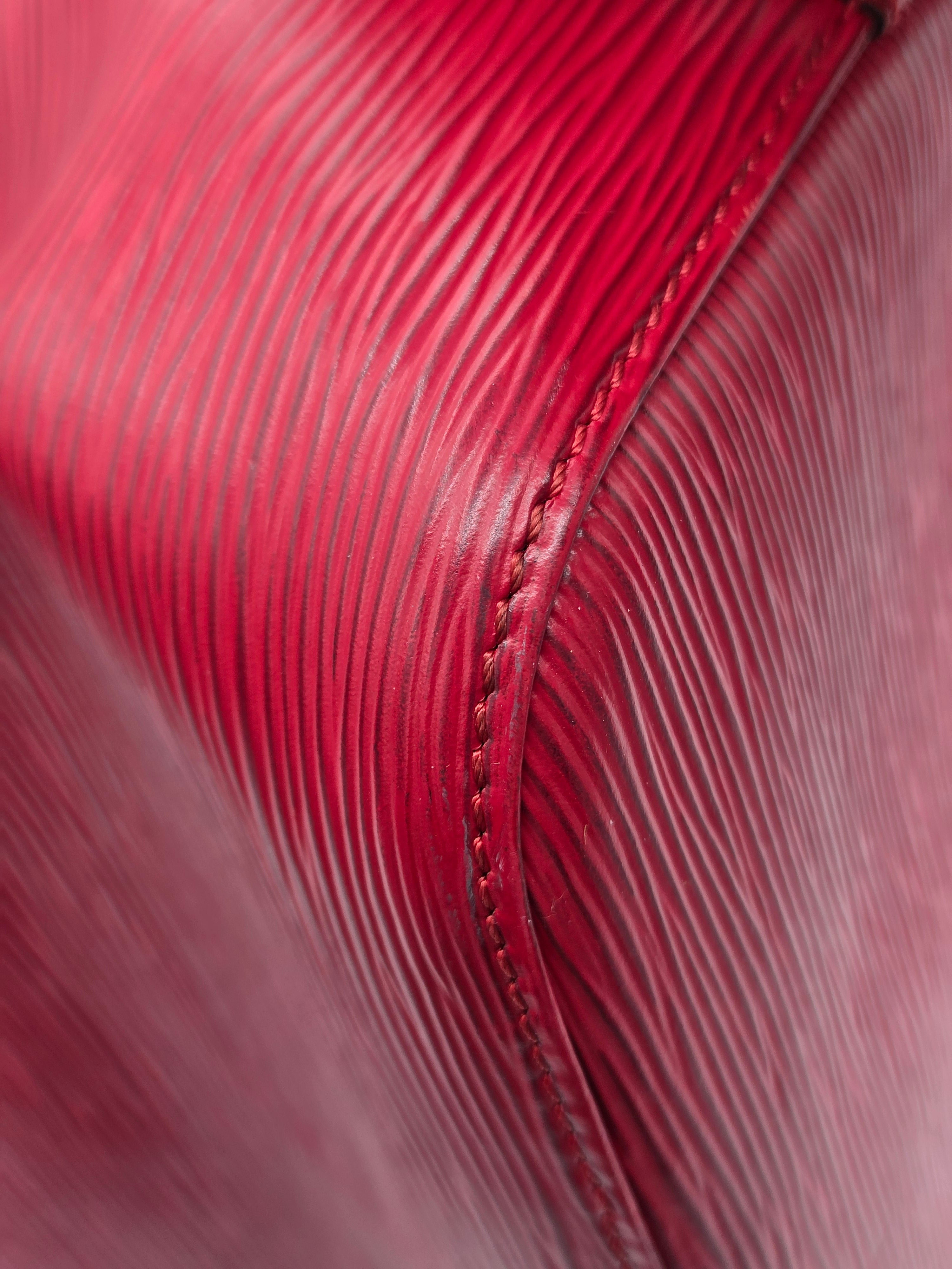 Close-up of a textured red leather surface with fine horizontal grain and a stitched seam.