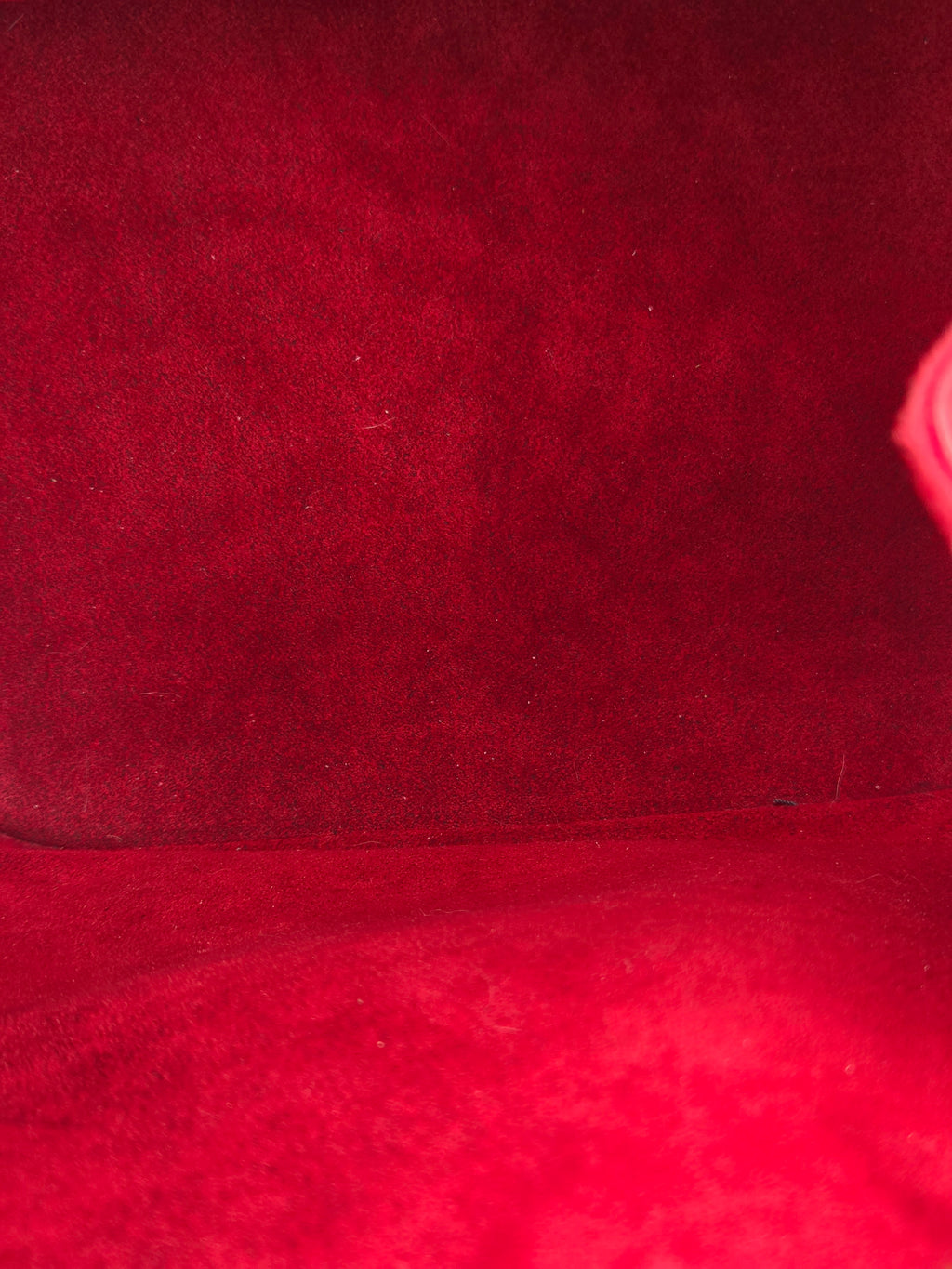 A close-up of a deep red suede or velvet fabric texture, showing the soft napped surface and a seam running vertically.