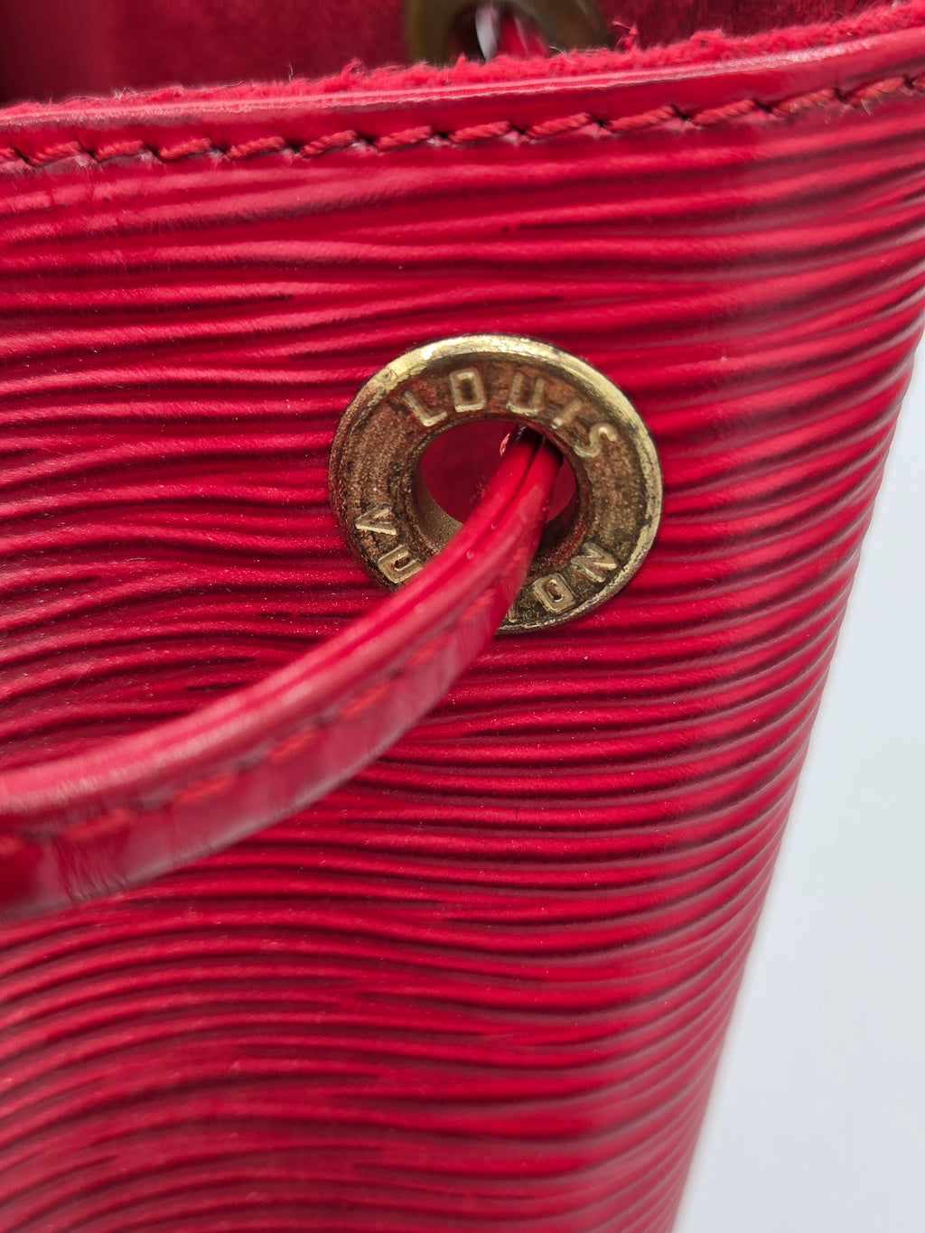 Close-up of a bright red textured leather bag with a gold-tone Louis Vuitton monogram ring detail on the strap.