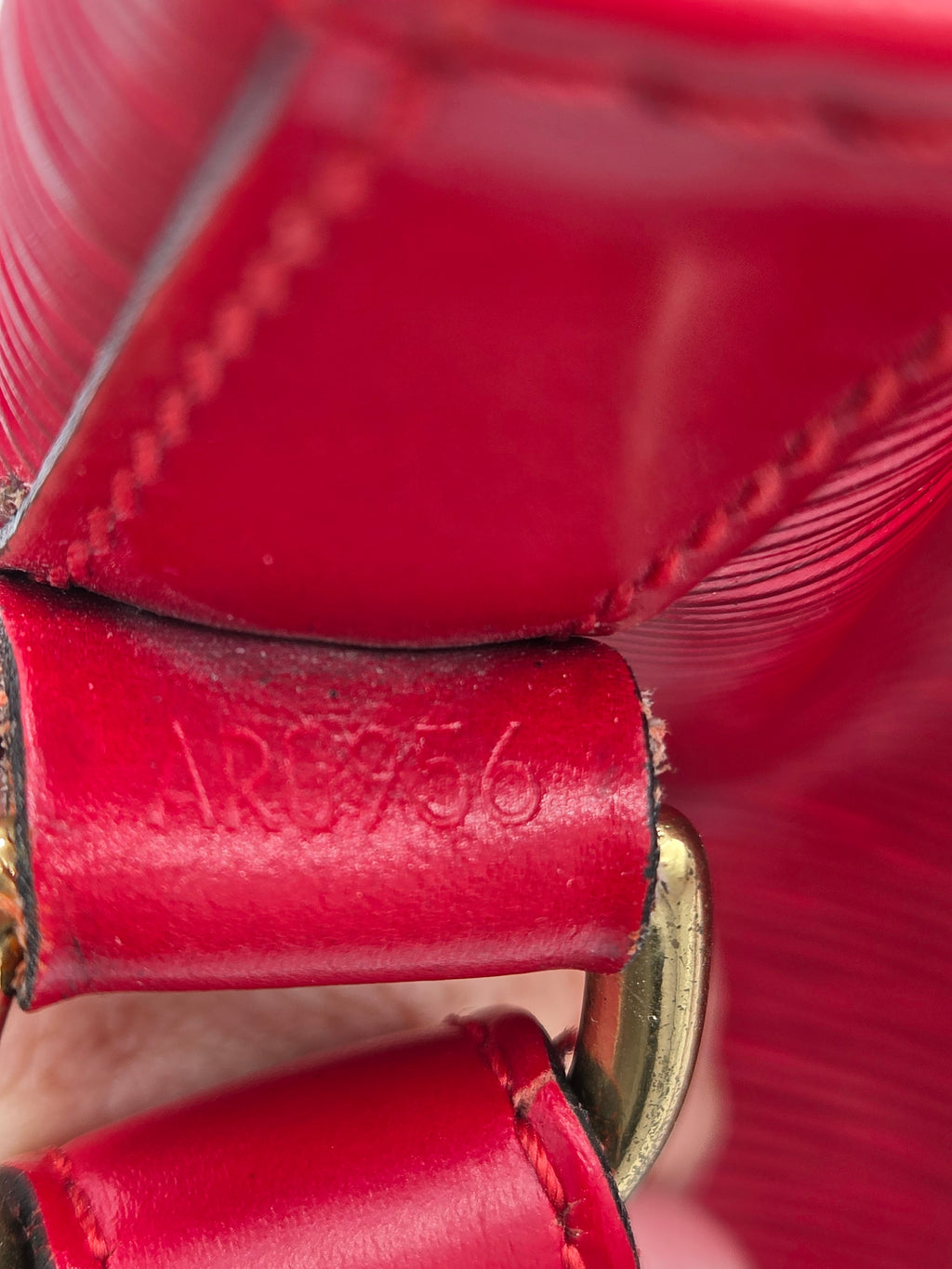 Close-up of a red leather strap with visible stitching, a brass metal loop, and an embossed '1876' detail on the leather tab.