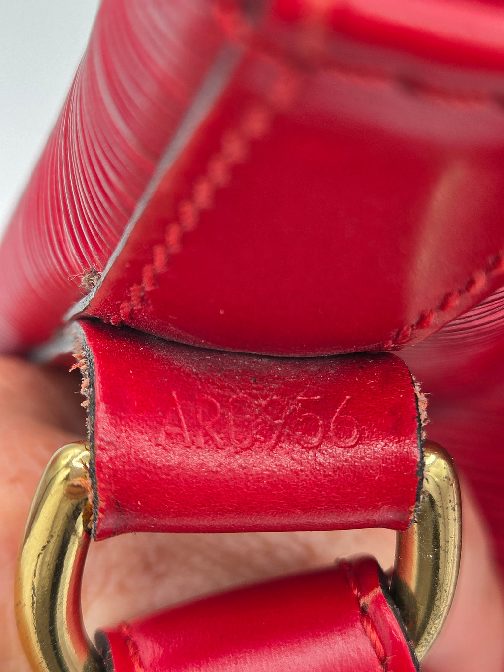 Close-up of a red leather strap with gold-tone metal hardware and a small embossed logo on the leather tab.