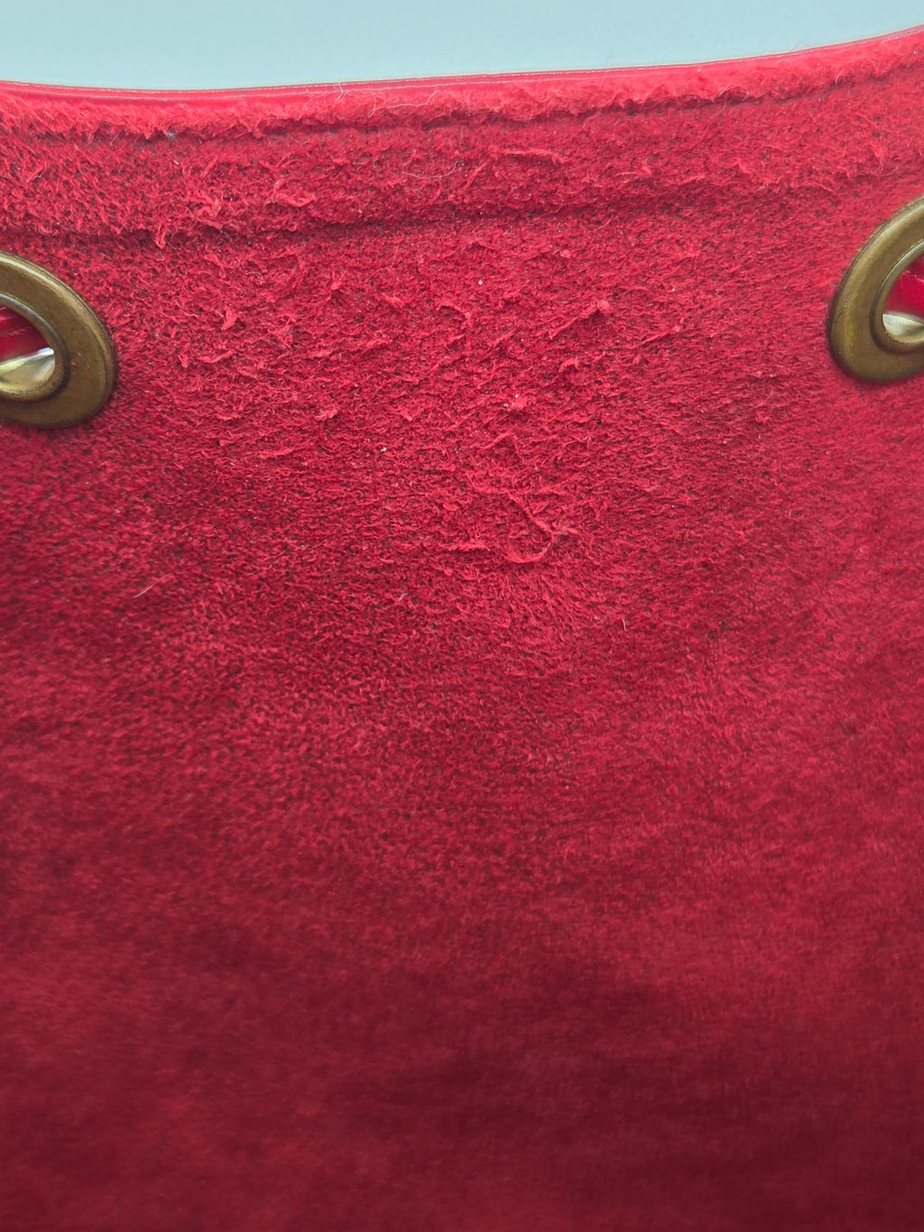 A close-up of a textured red fabric surface with two brass grommets visible along the left edge.