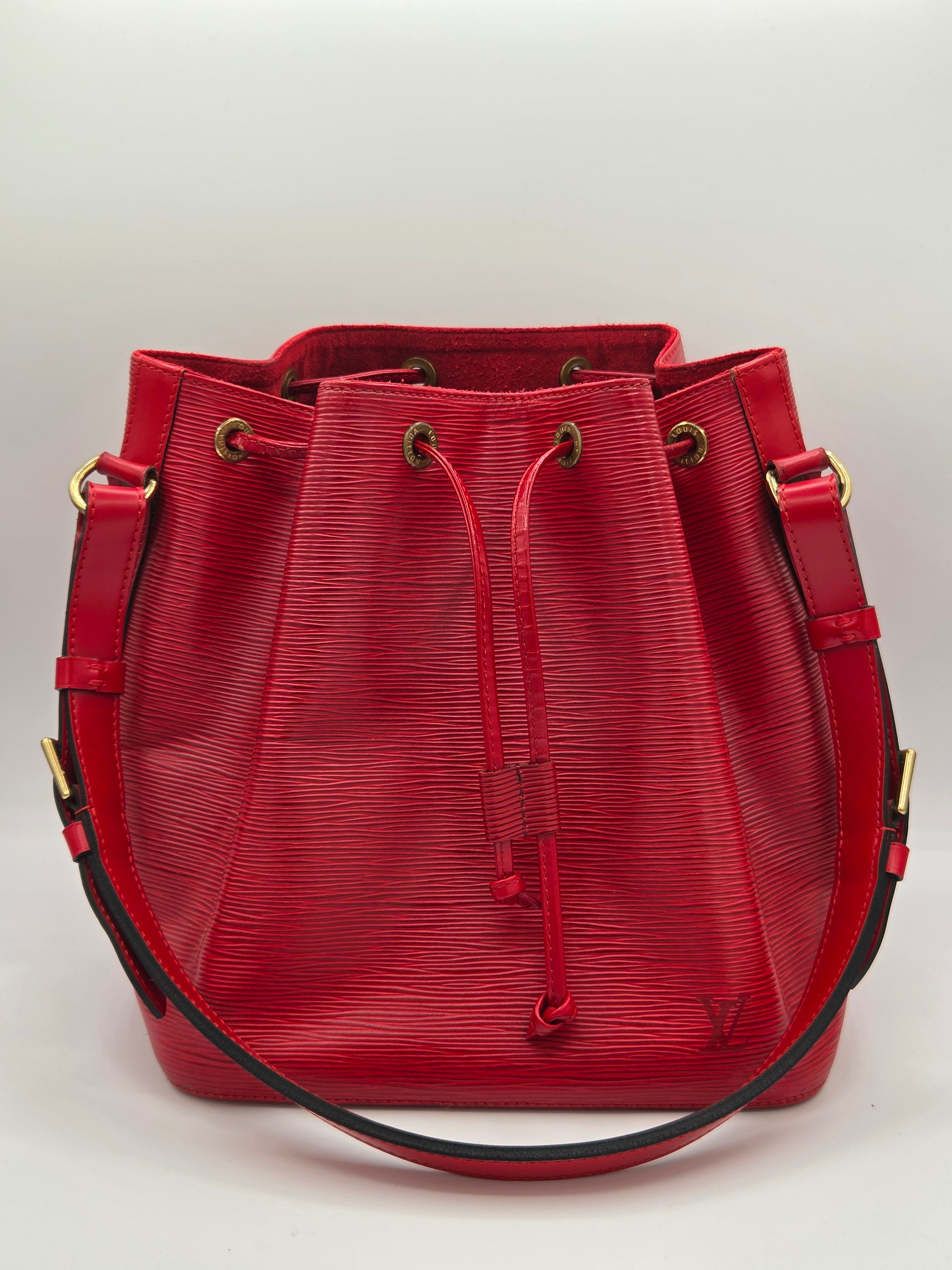 A red textured leather shoulder bag with a drawstring closure and gold-tone hardware, photographed from above on a light gray background.
