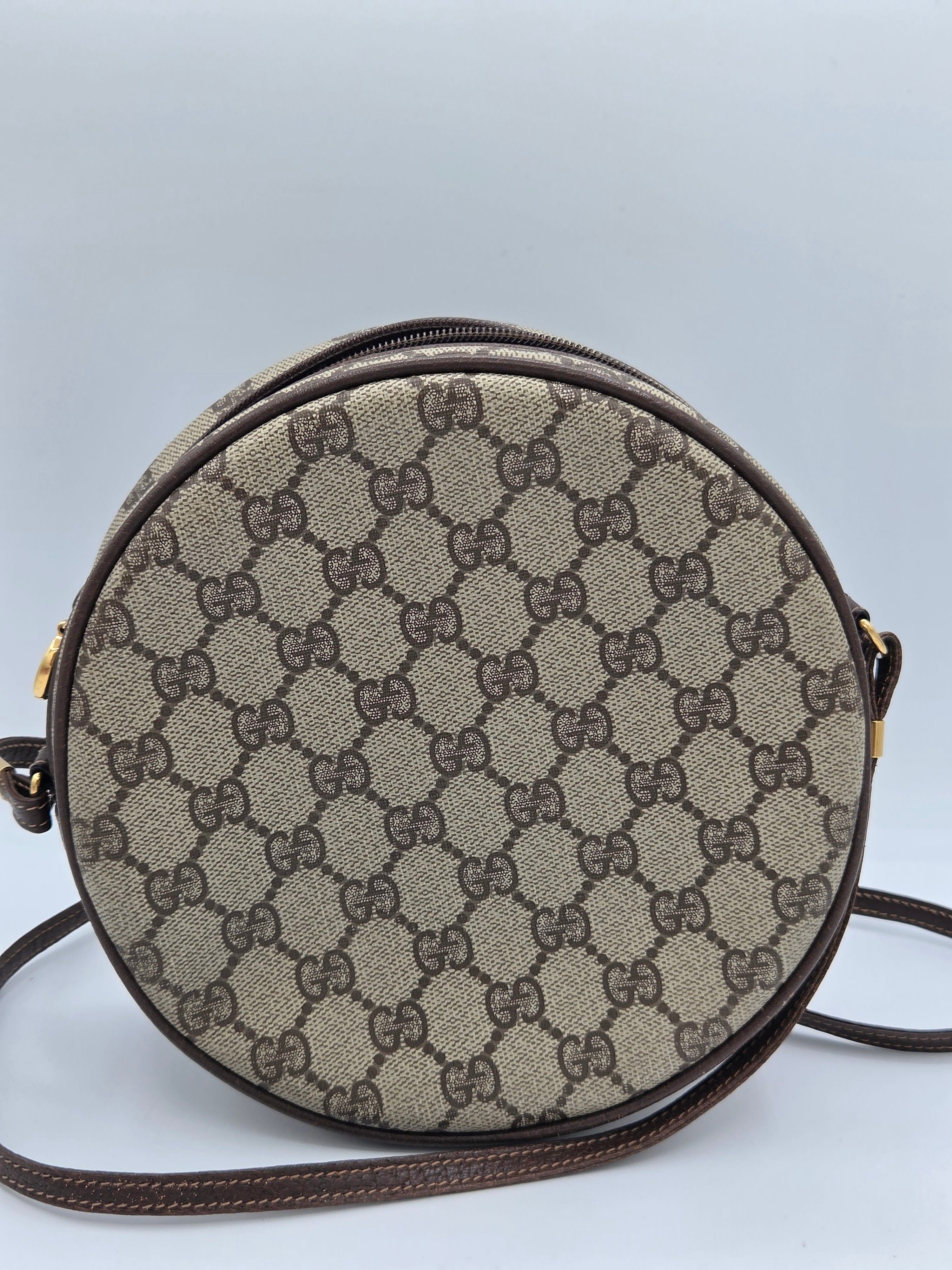 A round Gucci shoulder bag in the classic GG Supreme canvas, featuring a beige and brown monogram pattern with dark brown leather trim and strap.