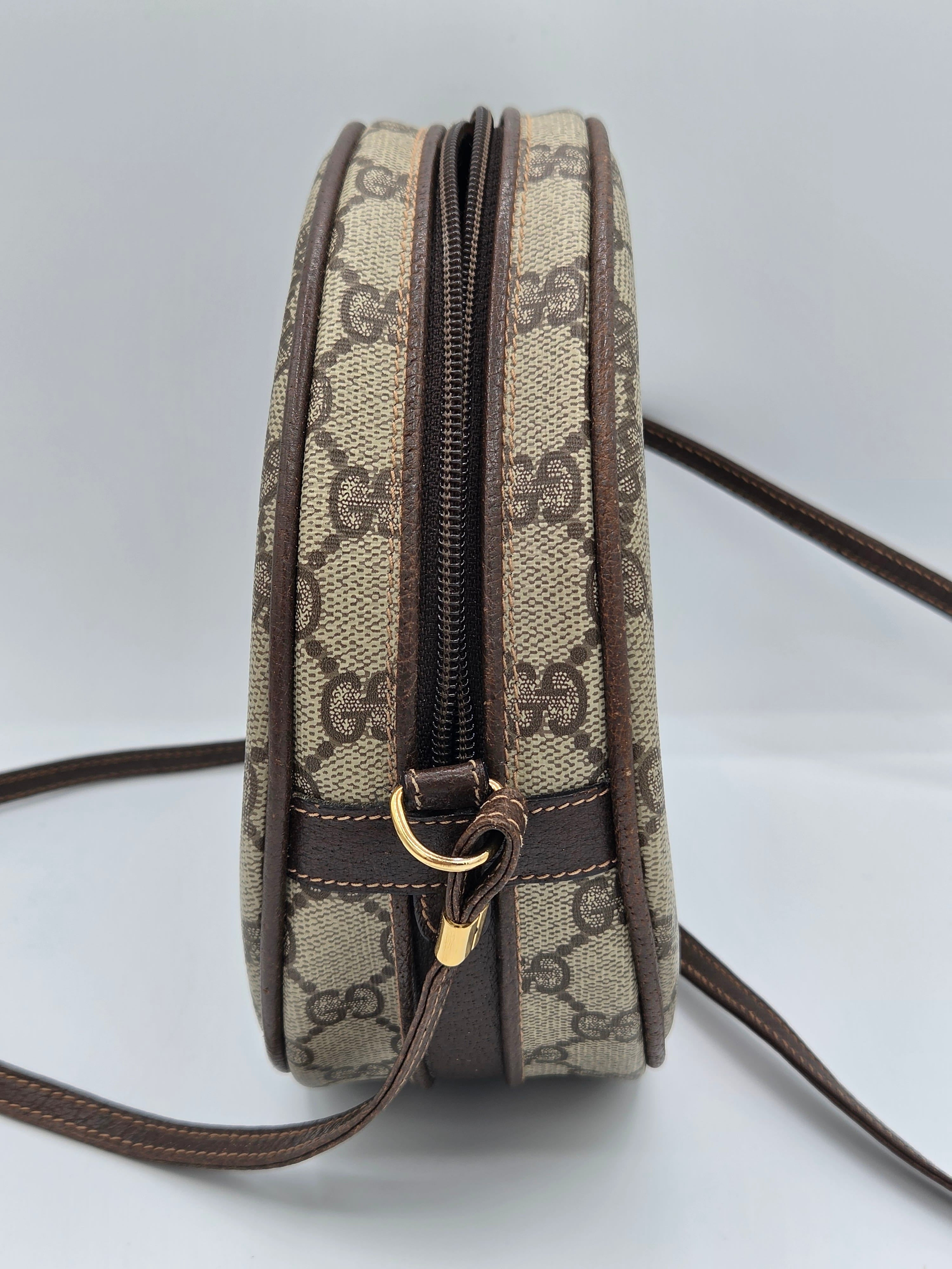 A Gucci monogram canvas crossbody bag with a brown leather trim and zipper, featuring the iconic GG pattern in beige and brown with gold-tone hardware.