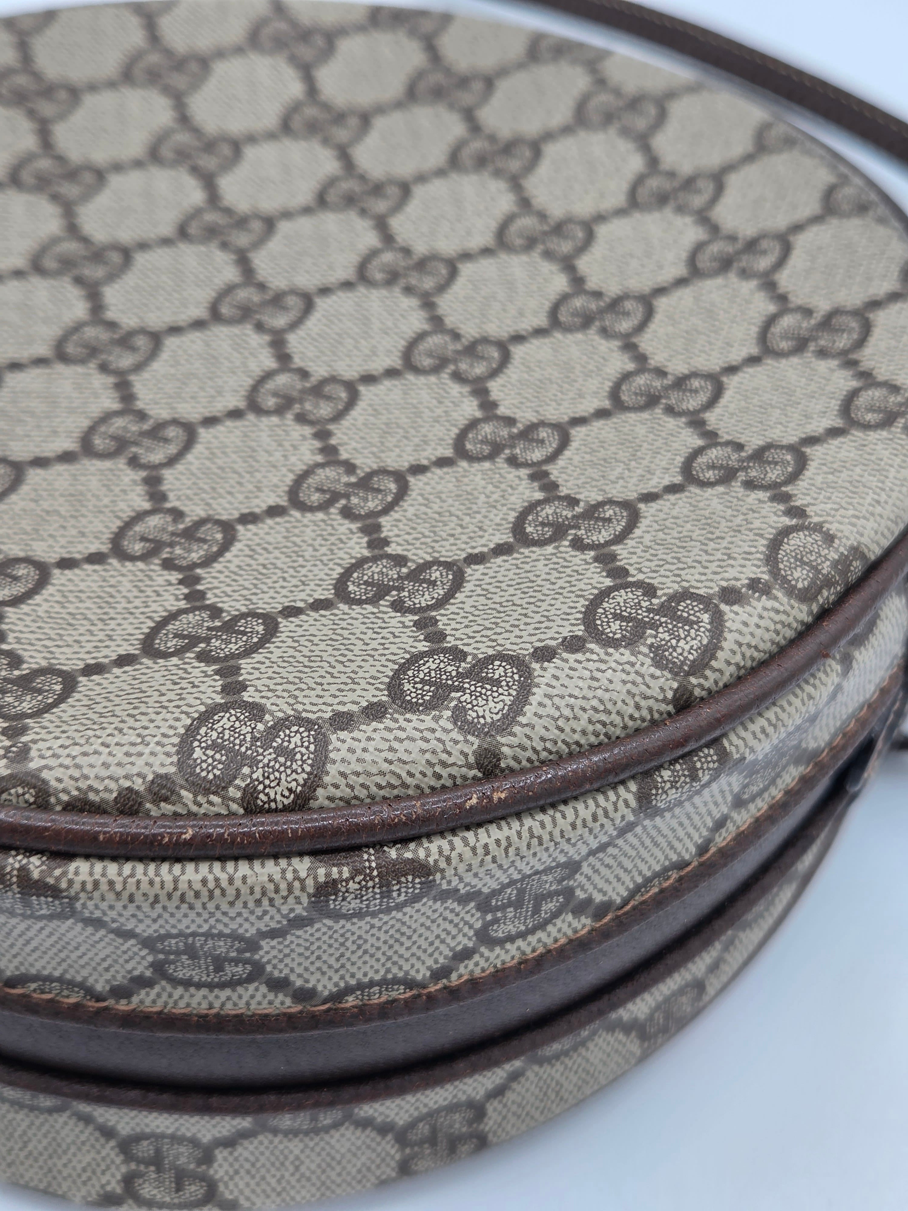 Close-up of a Gucci monogram canvas accessory, showing the signature GG pattern in beige and brown with dark brown leather trim.
