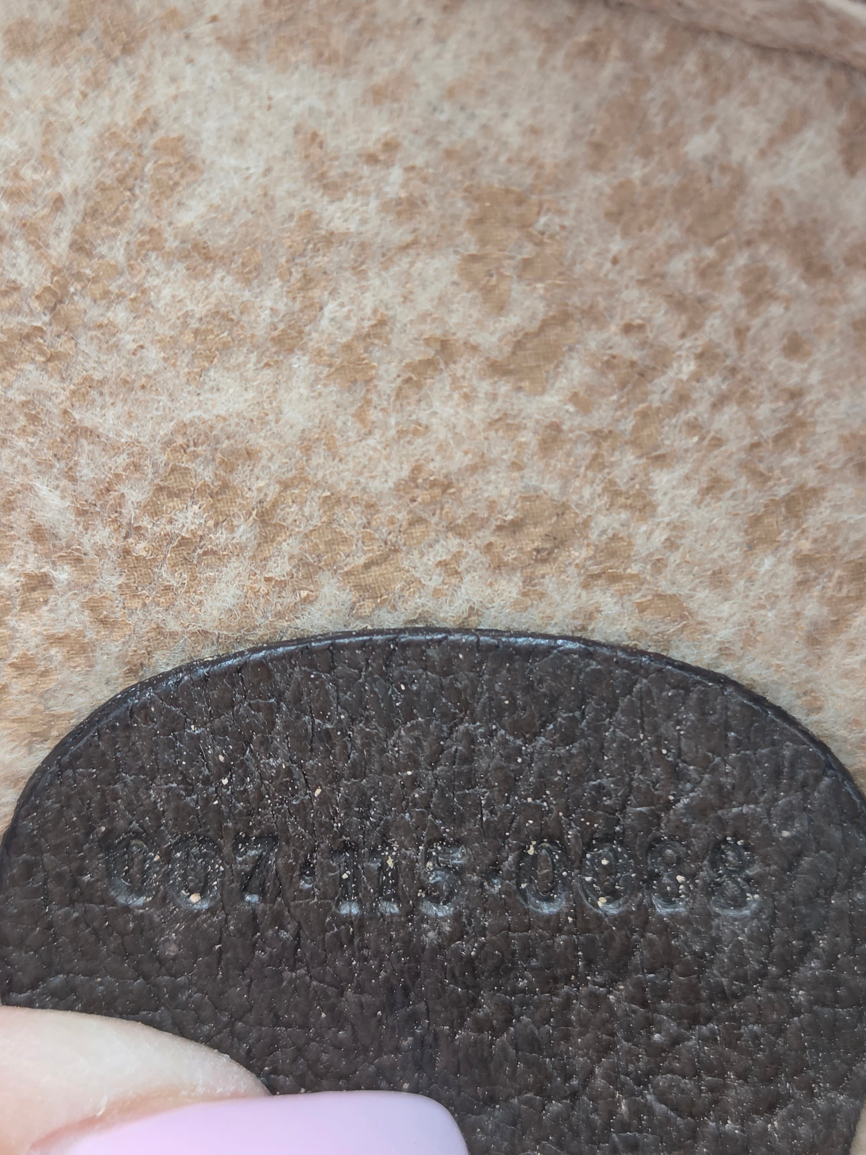Close-up of a dark brown textured leather patch with a small light pink fingernail visible at the edge against a beige fuzzy fabric background.