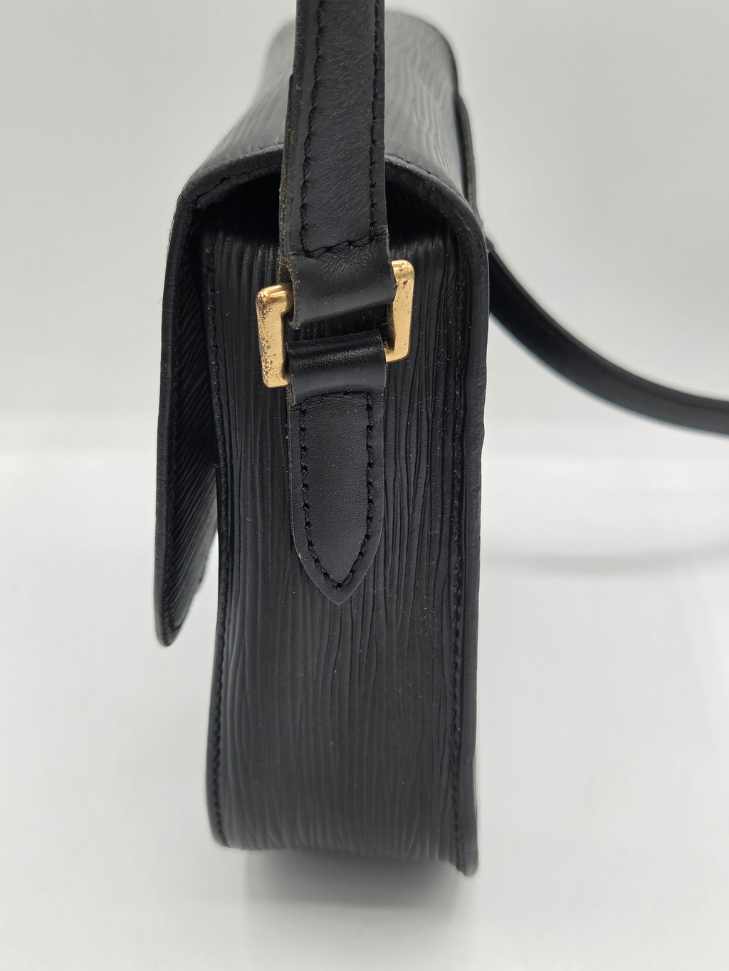 Close-up side view of a black textured leather handbag with gold-tone hardware and a black strap on a white background.