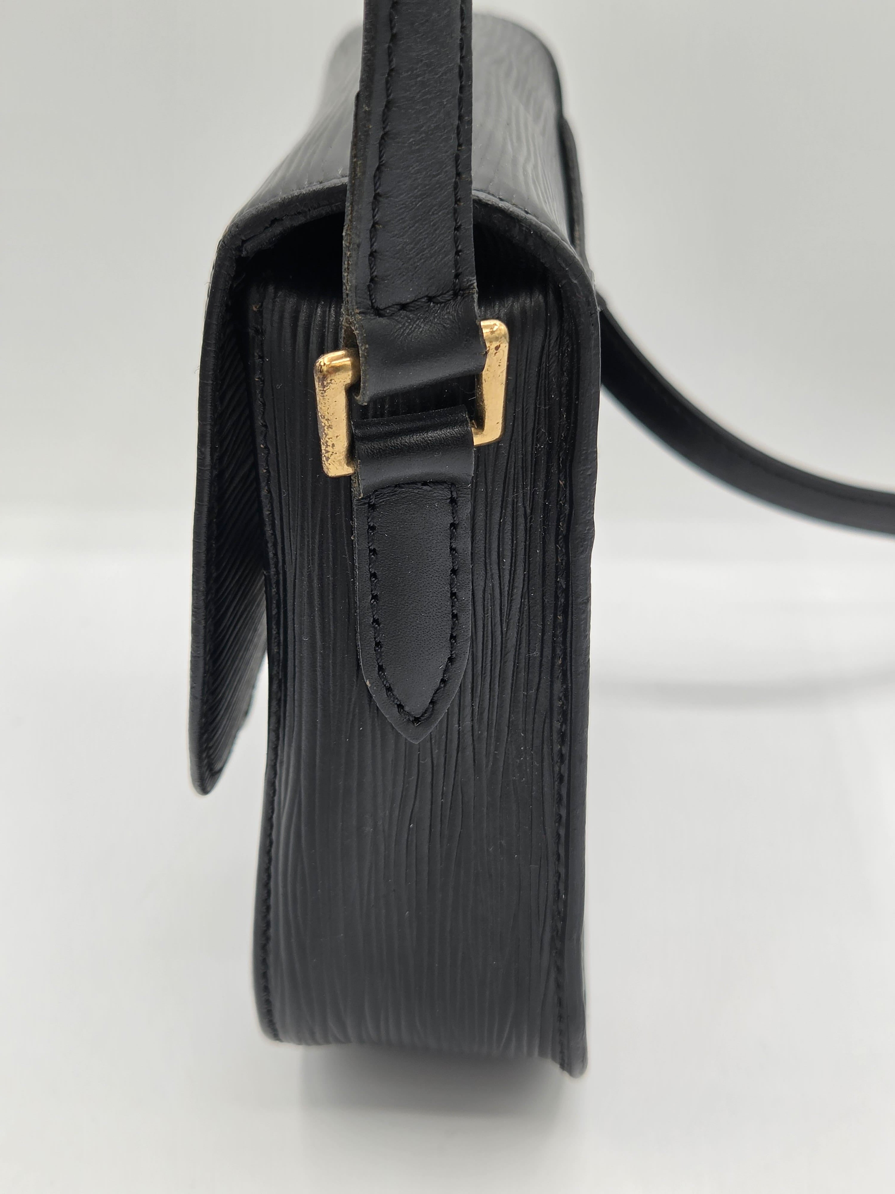 Close-up side view of a black textured leather handbag with gold-tone hardware and a black strap on a white background.