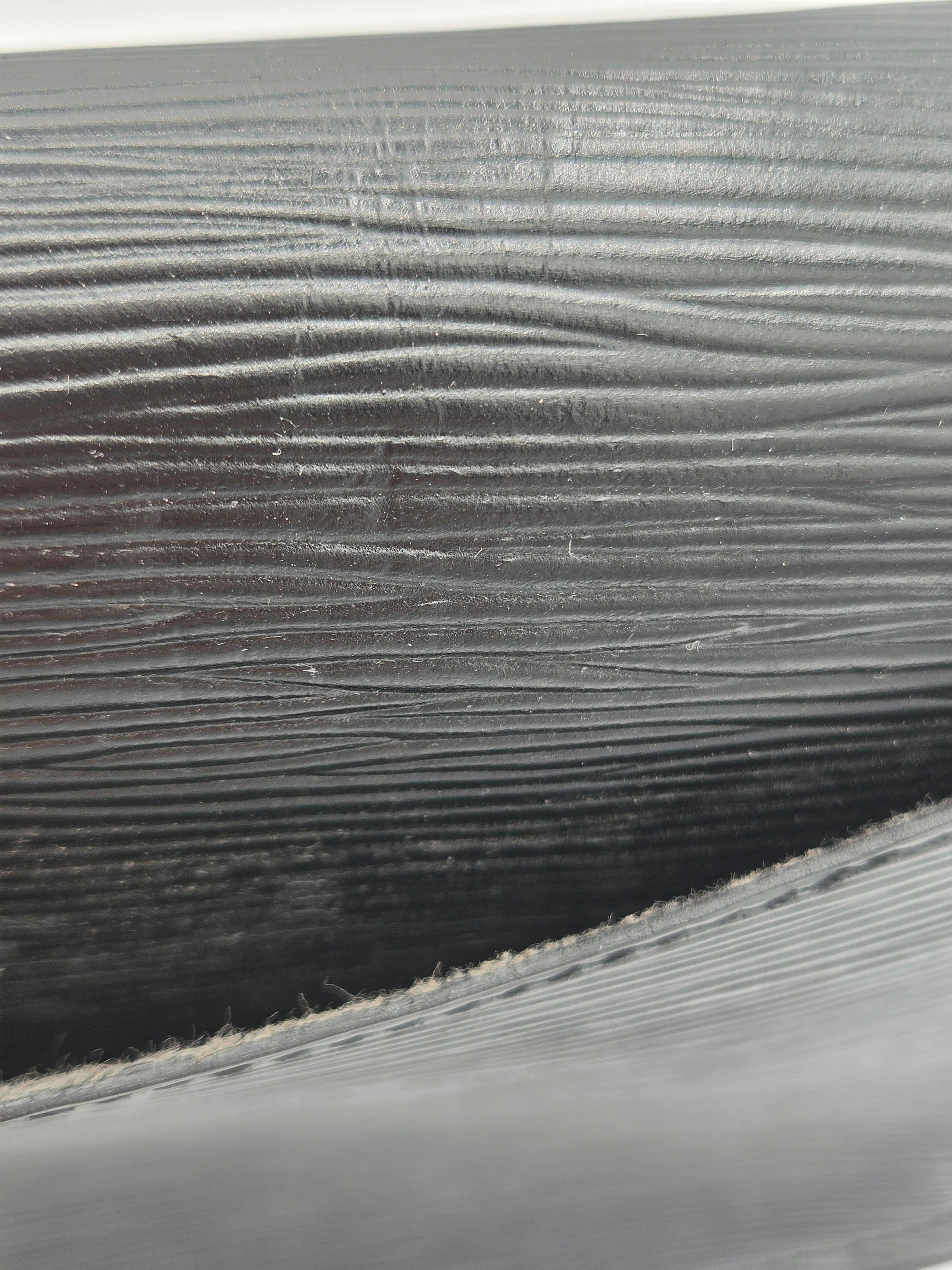 Close-up of a dark gray or black textured material with horizontal ridges and a stitched edge visible in the lower foreground.