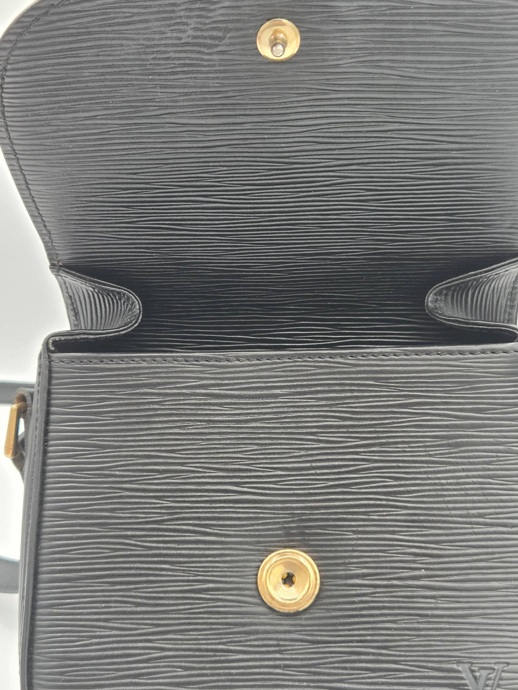 Close-up of a dark gray textured leather handbag interior showing a gold-tone snap button and the embossed Louis Vuitton monogram at the bottom right corner.