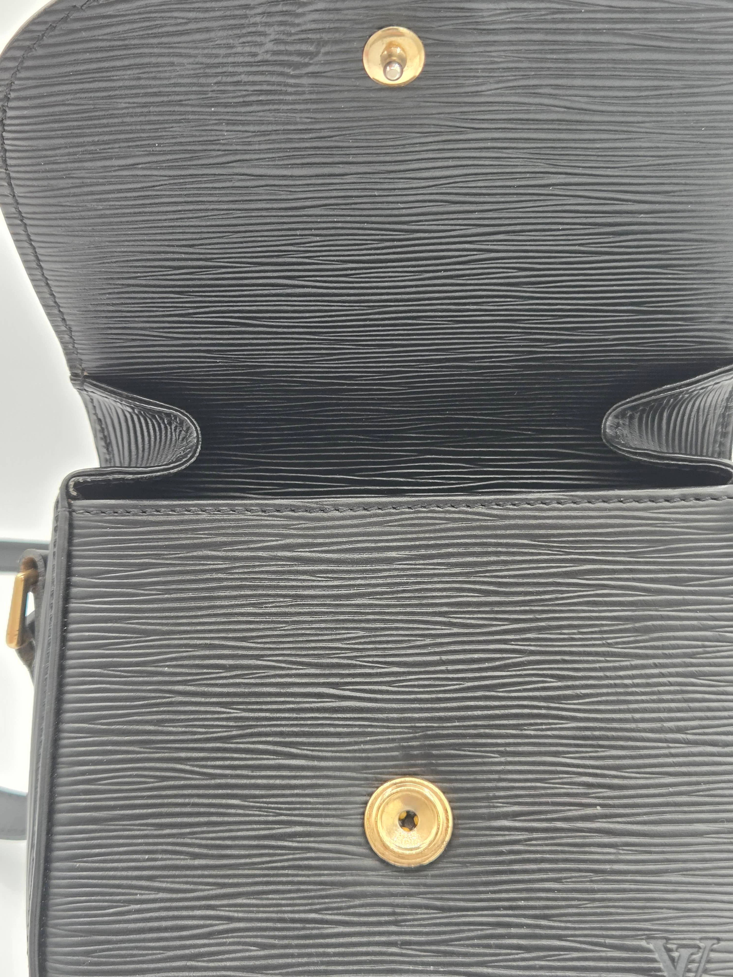 Close-up of a dark gray textured leather handbag interior showing a gold-tone snap button and the embossed Louis Vuitton monogram at the bottom right corner.