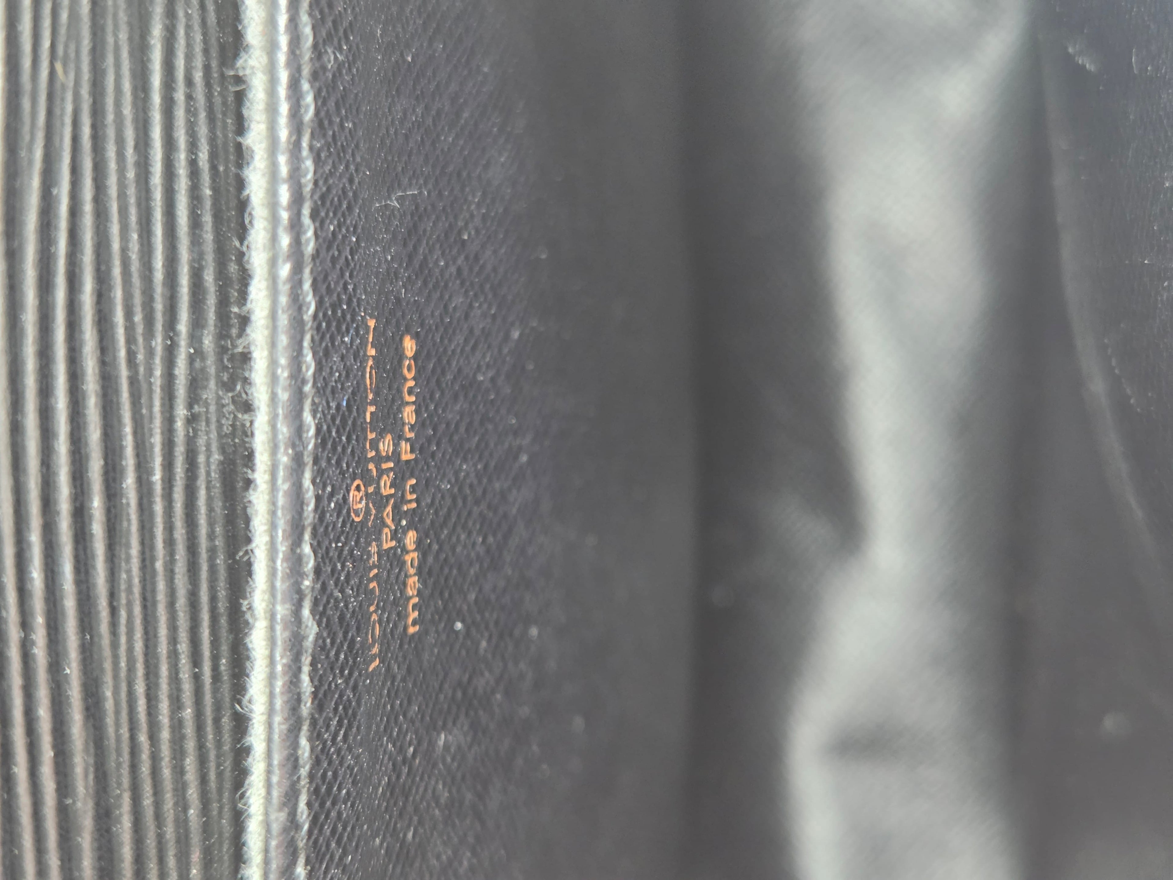 Close-up of a dark gray textured fabric with vertical ribbed stitching on the left and small orange text reading 'MADE IN FRANCE' and '100% COTTON'.