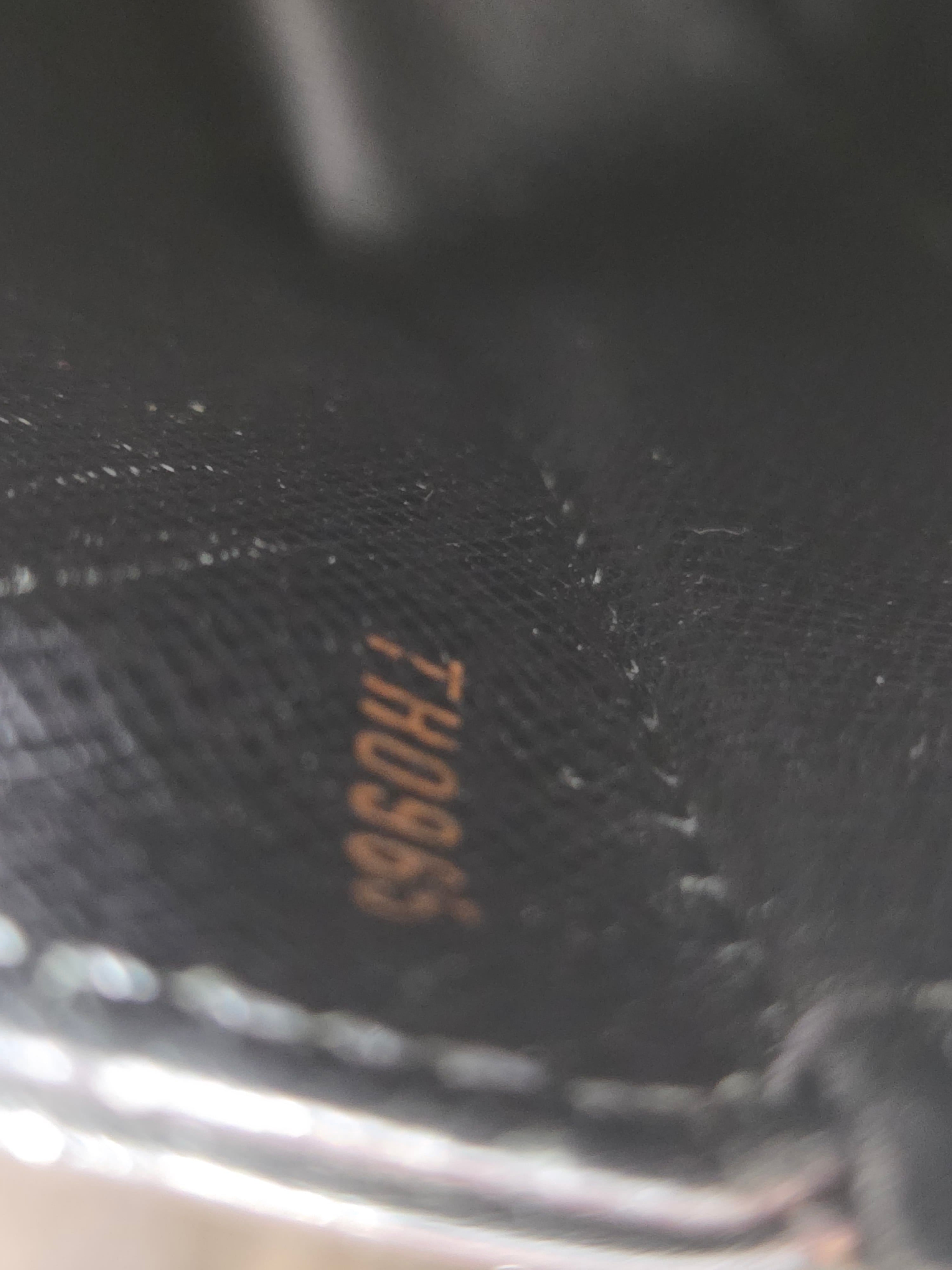 Close-up of a black textured leather surface with small gold stamped characters reading 'TH0963'.