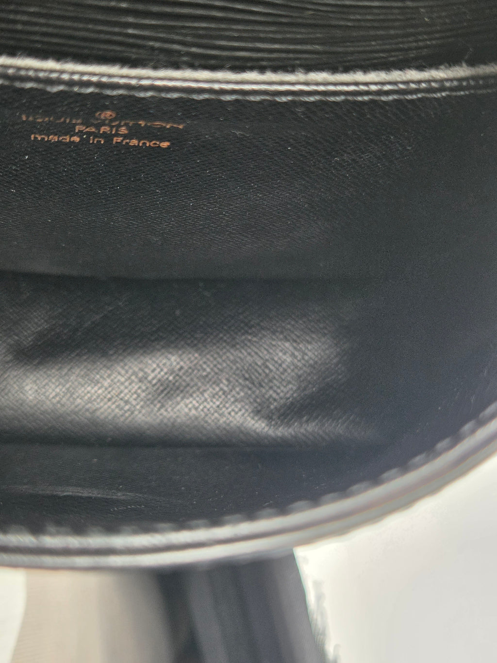 Close-up of the interior lining of a black handbag, showing the printed text 'Louis Vuitton Paris France made in France' on black textured fabric.