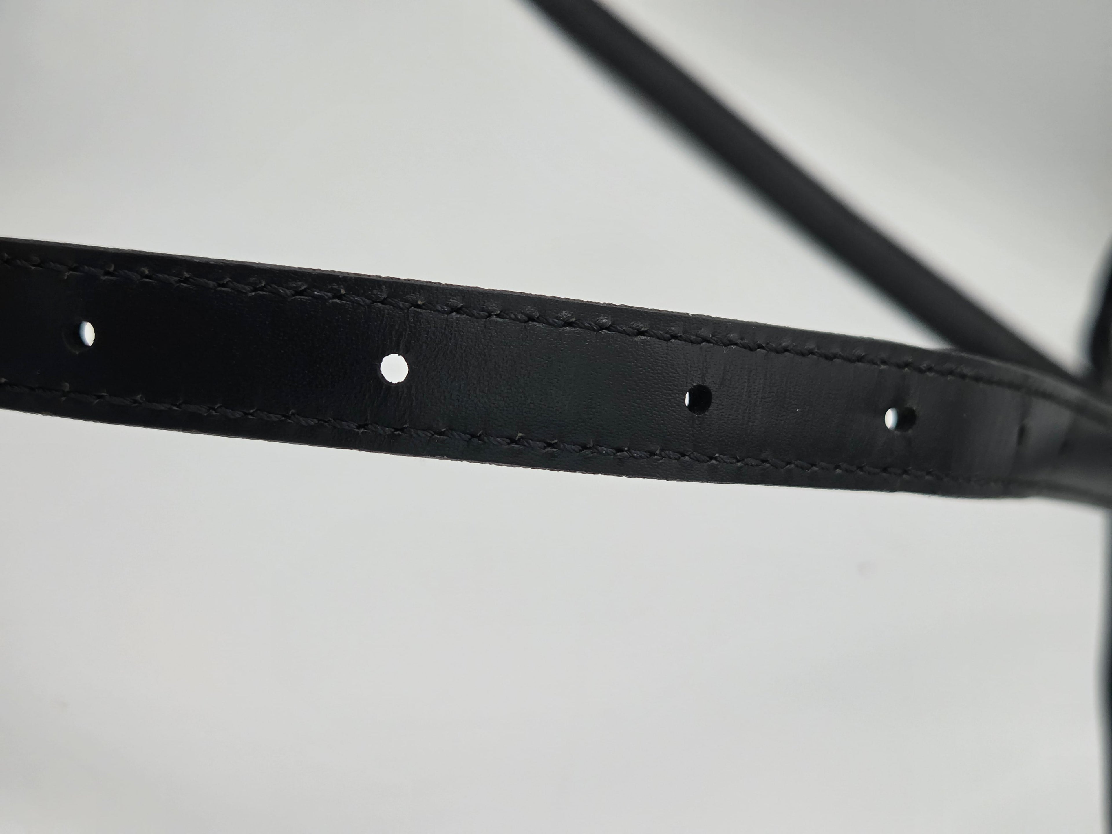 Close-up of a black leather strap with pre-drilled holes and fine stitching, shown against a light gray background.