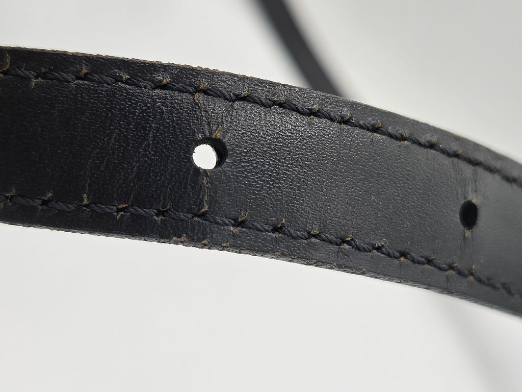 Close-up of a black leather strap with visible stitching and metal eyelets on a light gray background.