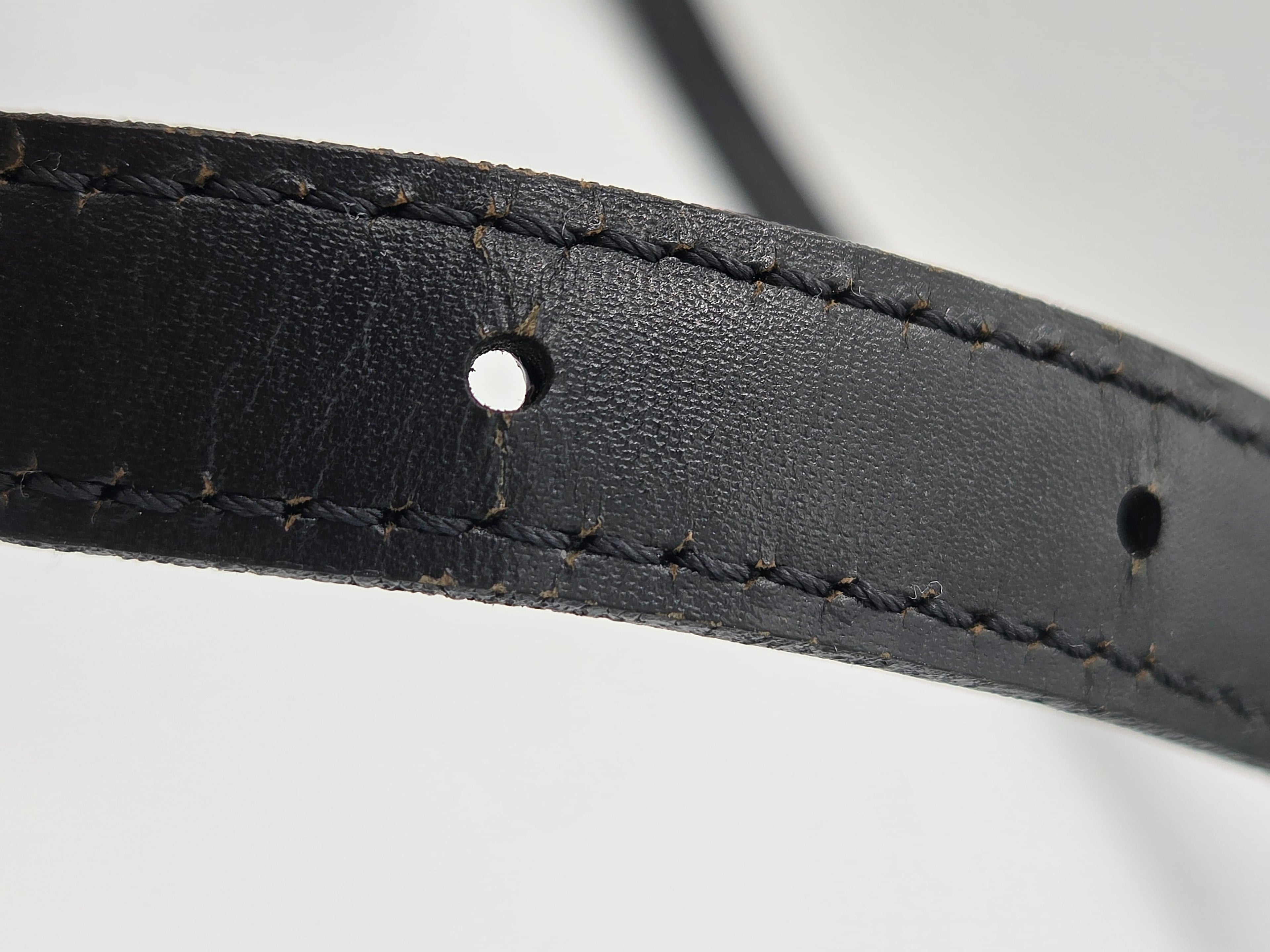 Close-up of a black leather strap with visible stitching and metal eyelets on a light gray background.