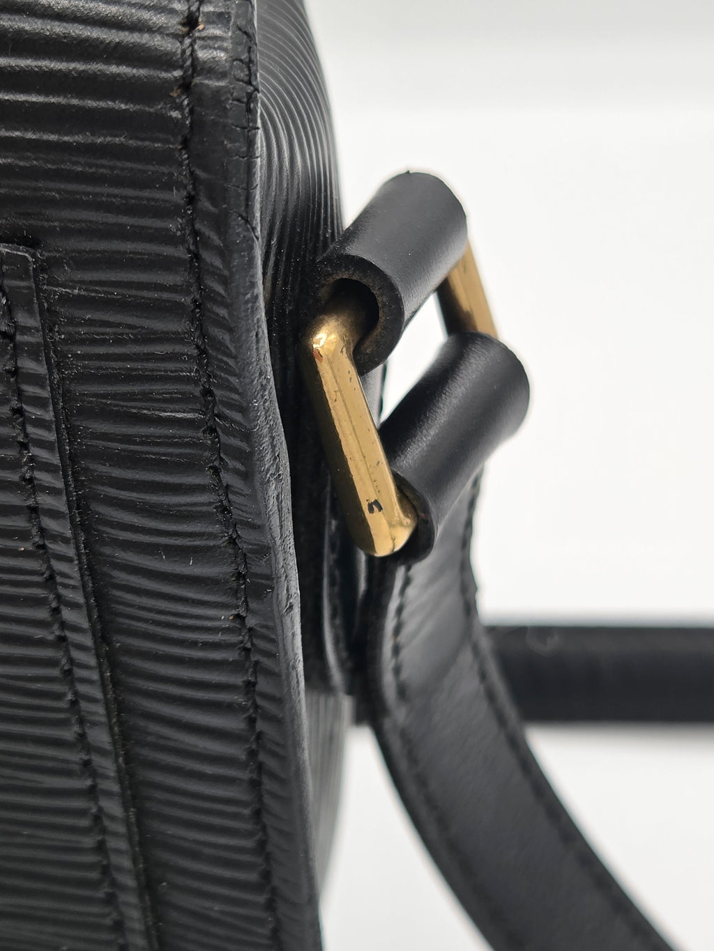 Close-up of a black textured leather handbag strap with a gold-tone metal buckle, showing the detailed stitching and material texture.