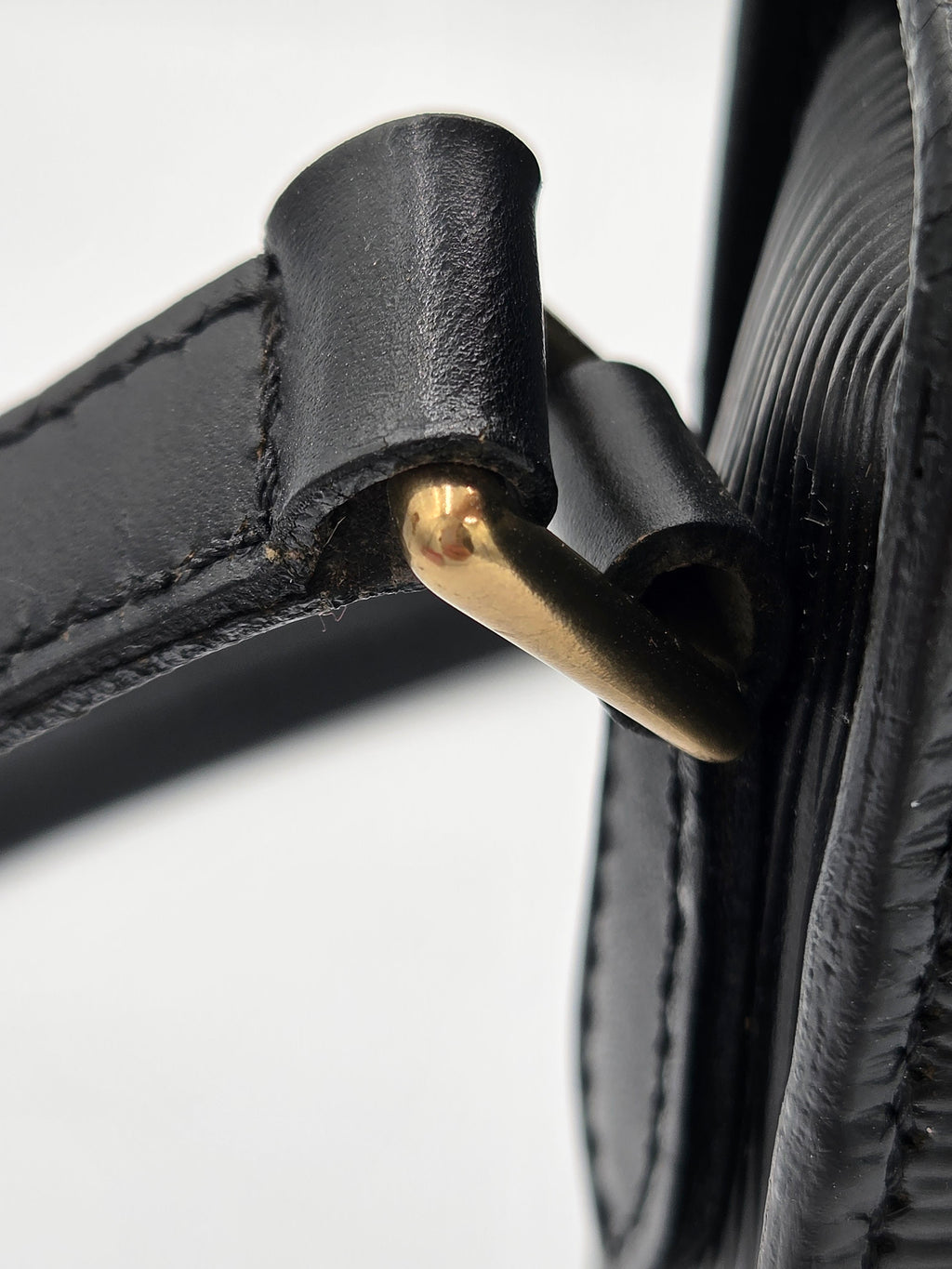 Close-up detail of a black leather strap with gold-tone metal hardware on a light gray background.
