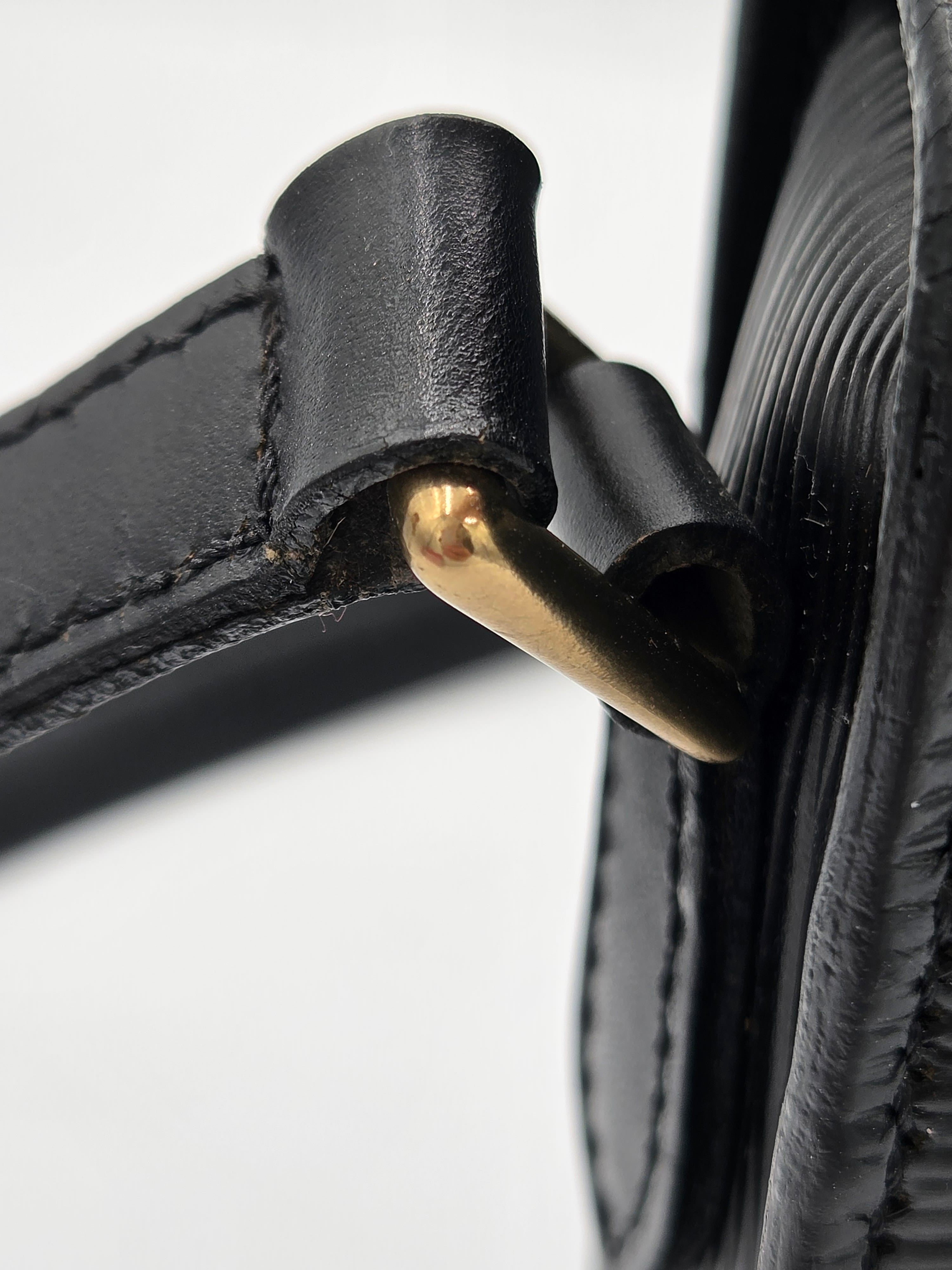 Close-up detail of a black leather strap with gold-tone metal hardware on a light gray background.